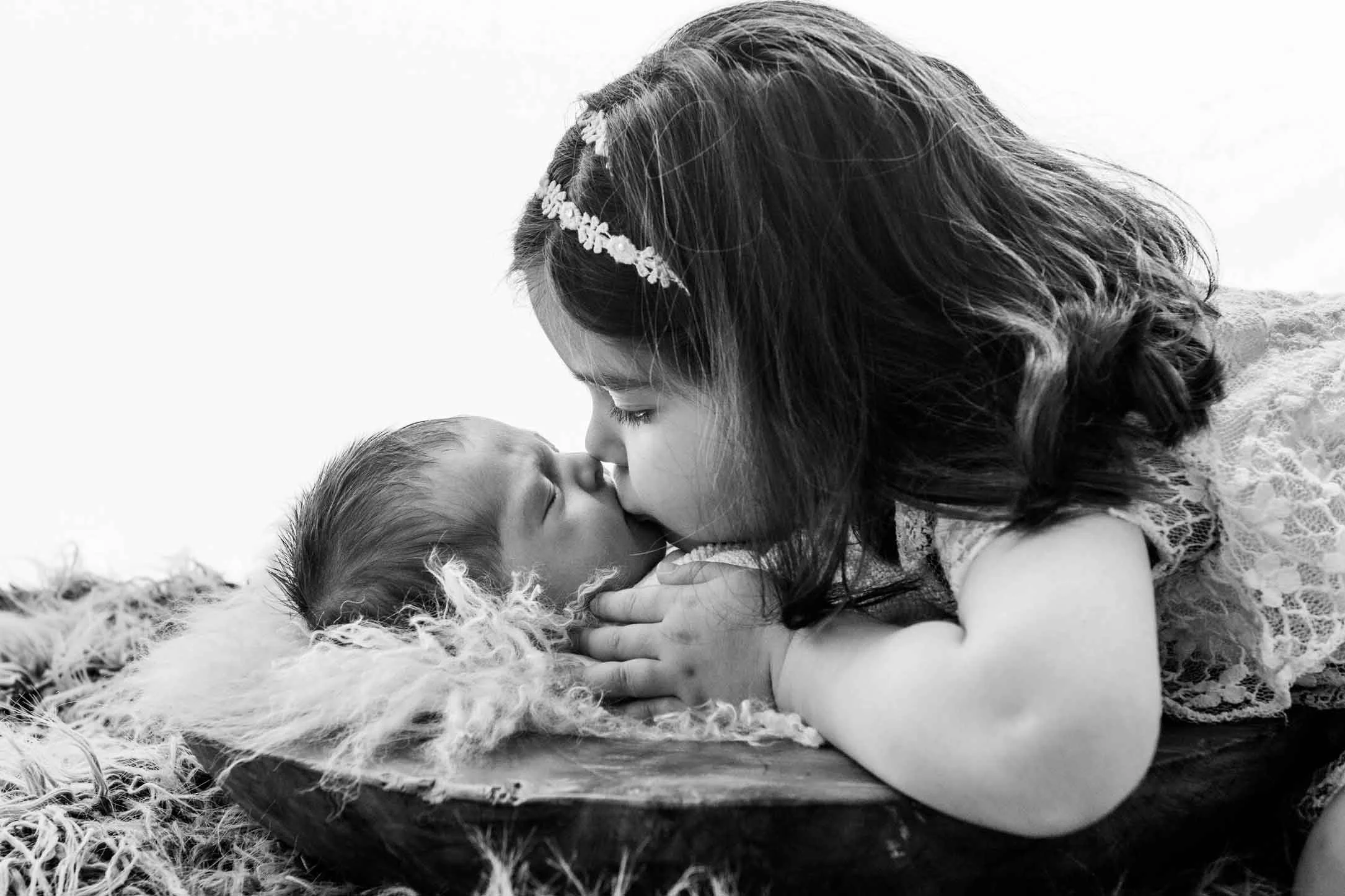 Eine ältere Schwester küsst ein neugeborenes Baby liebevoll auf die Stirn. Schwarzweiss Foto