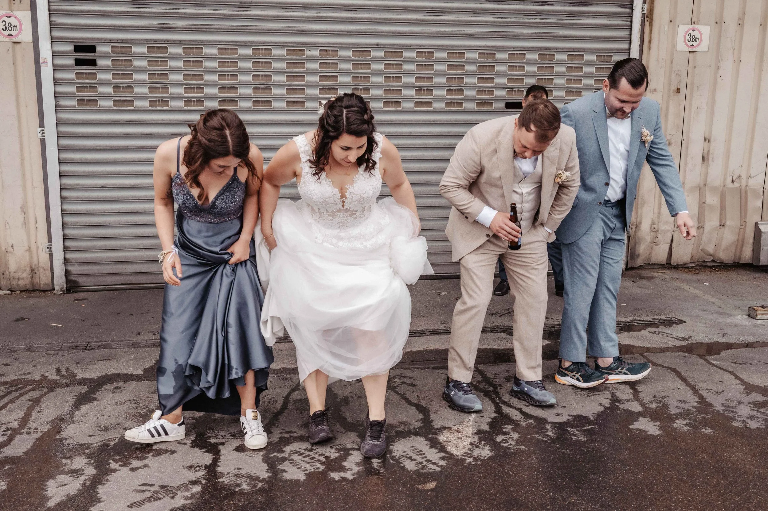 Brautpaar und Trauzeugen tanzen in Sneakers auf nasse Strasse, schauen auf den Boden.