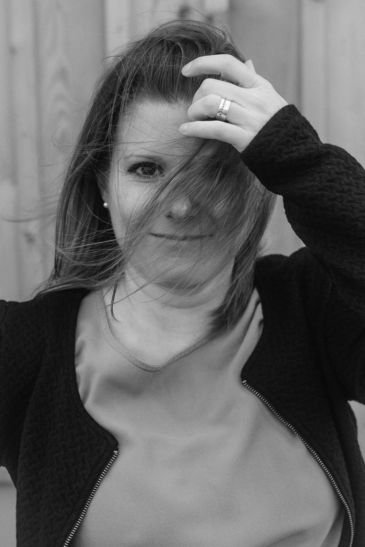 Schwarz-weiss-Foto von Janine Huber. Sie lacht in die Kamera und streicht Haare aus Gesicht.