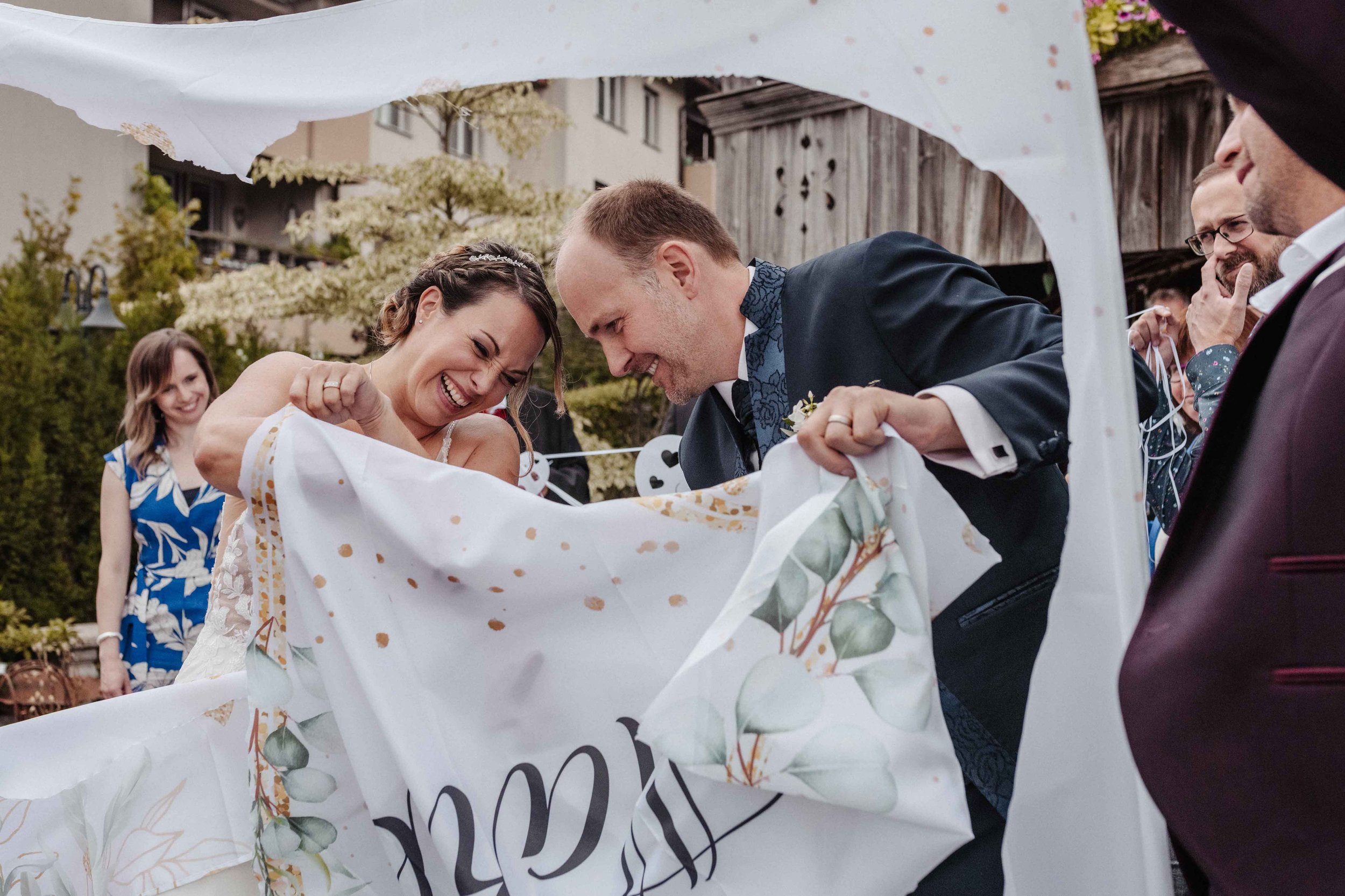Brautpaar schneidet bei Spalier ein Herz in Tuch.