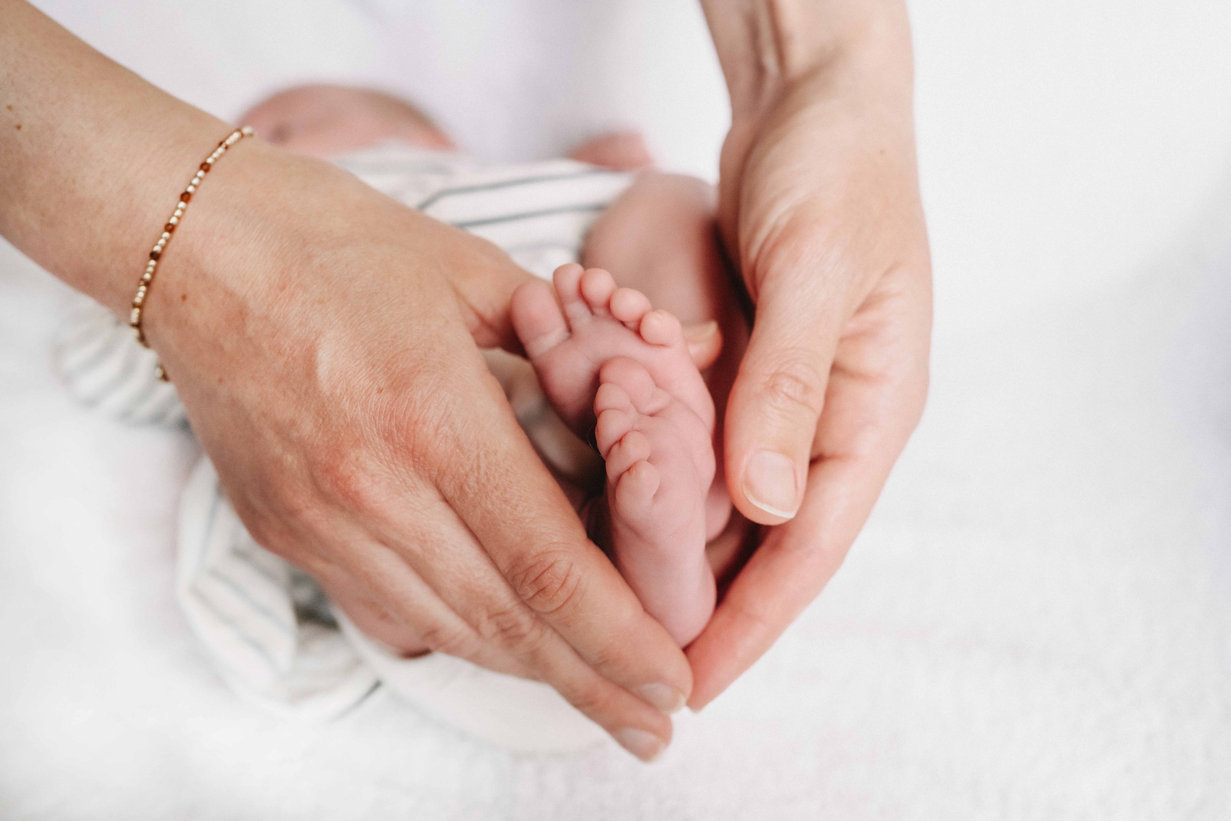 Mamas Hände halten die Füsse eines Babys.