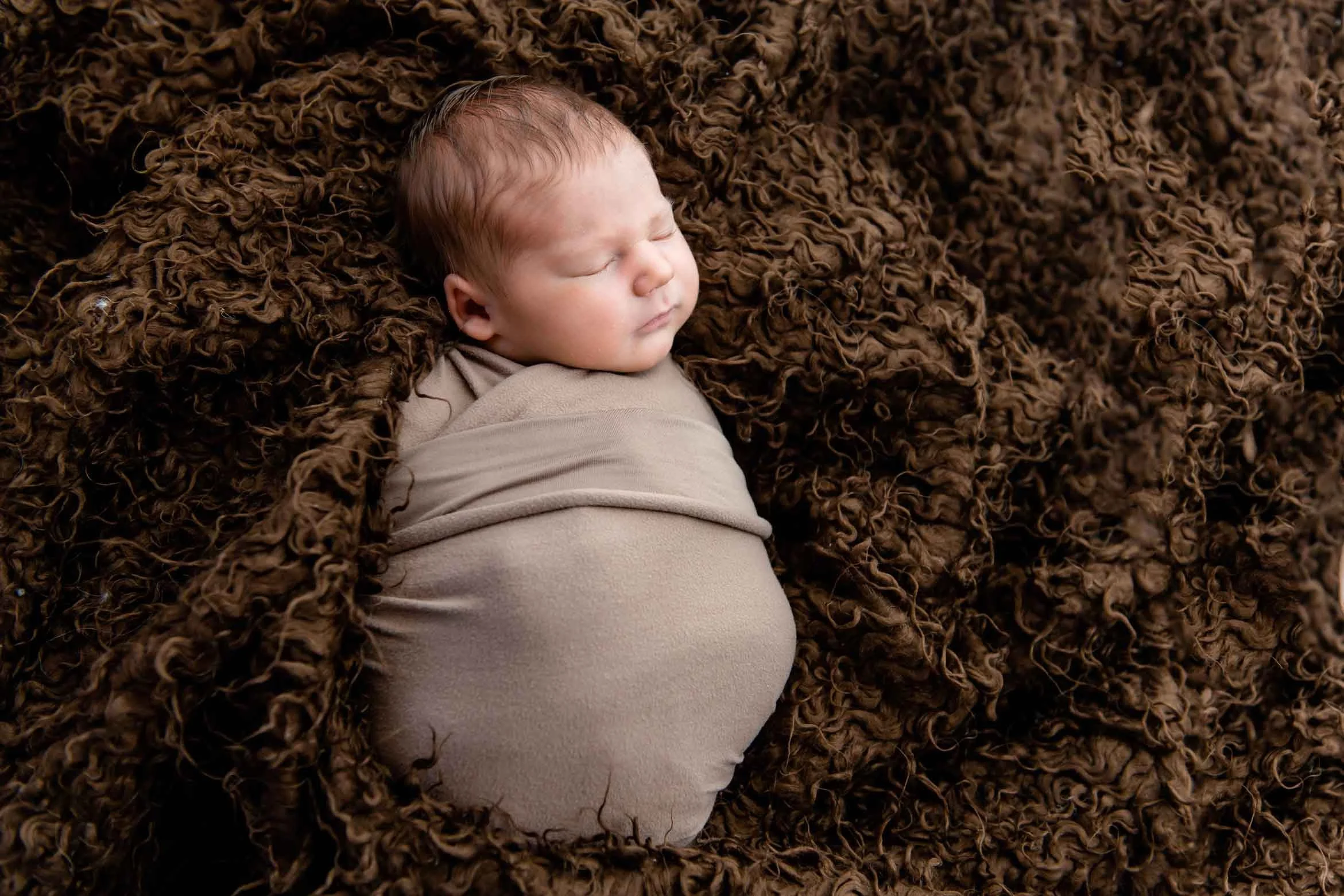 Baby liegt auf braunem Tuch.
