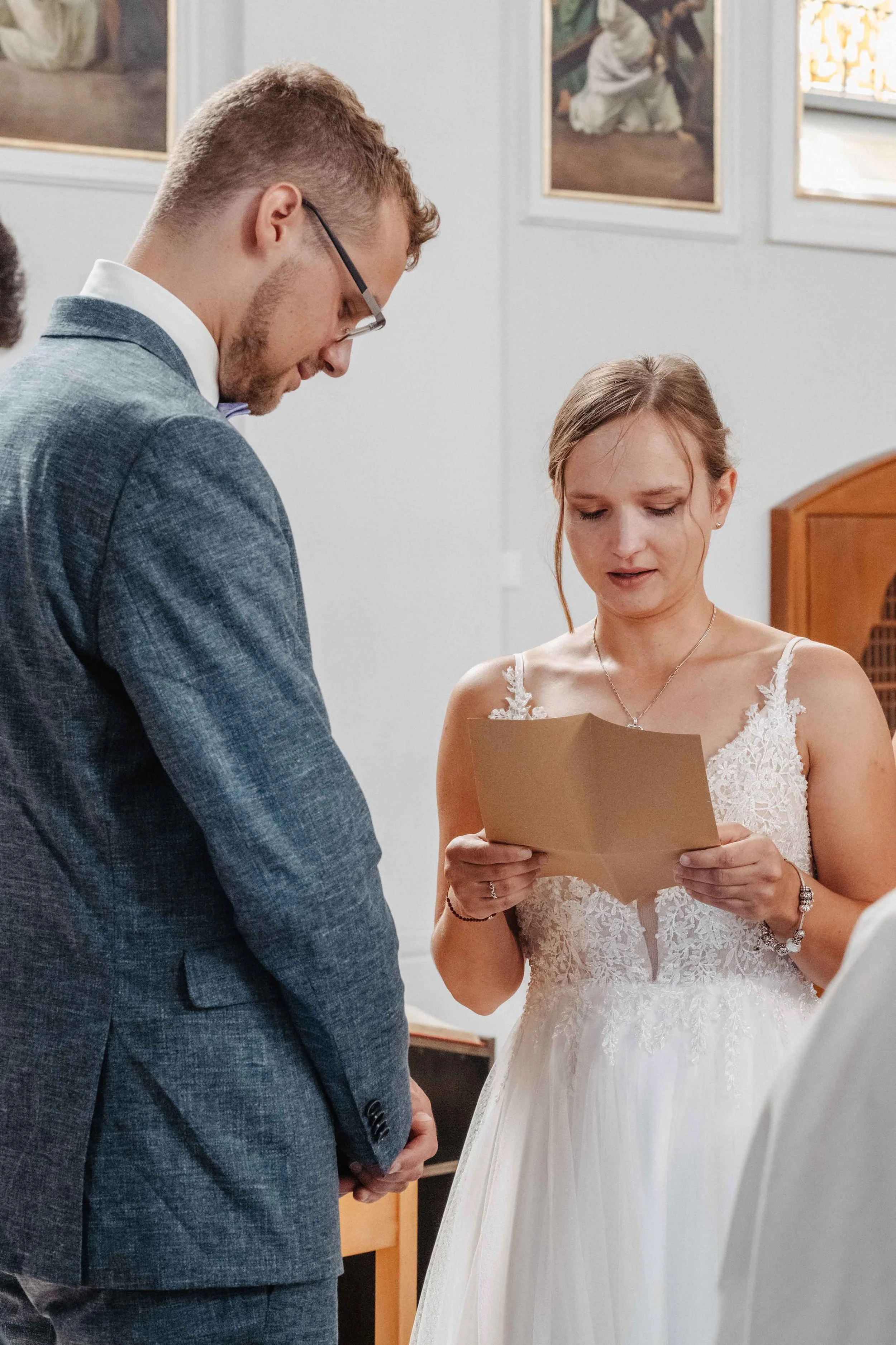 Braut liest während der kirchlichen Trauung persönliche Worte vor, während der Bräutigam zuhört.