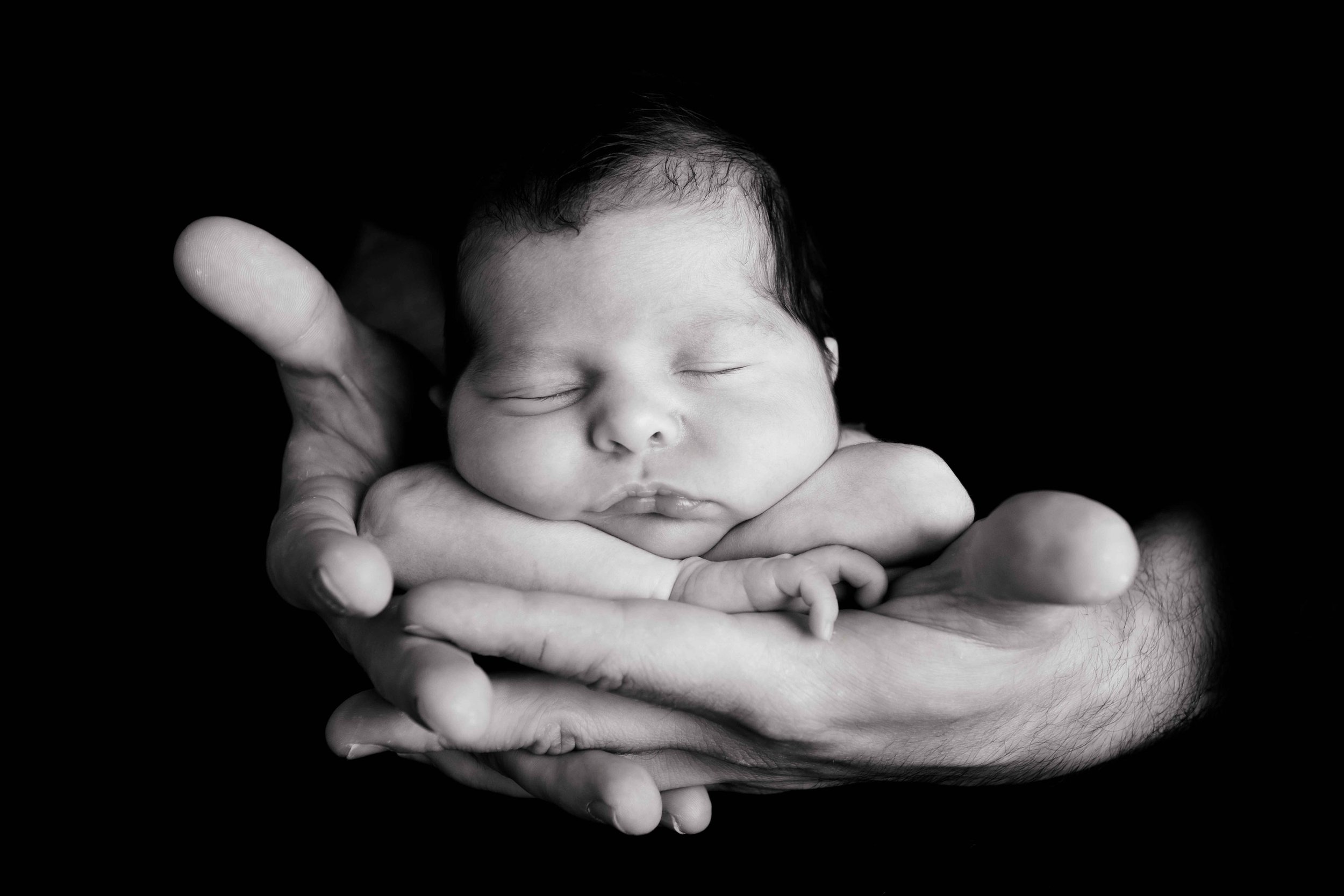 Schwarz-Weiss-Foto eines schlafenden Babys, das in Händen gehalten wird.