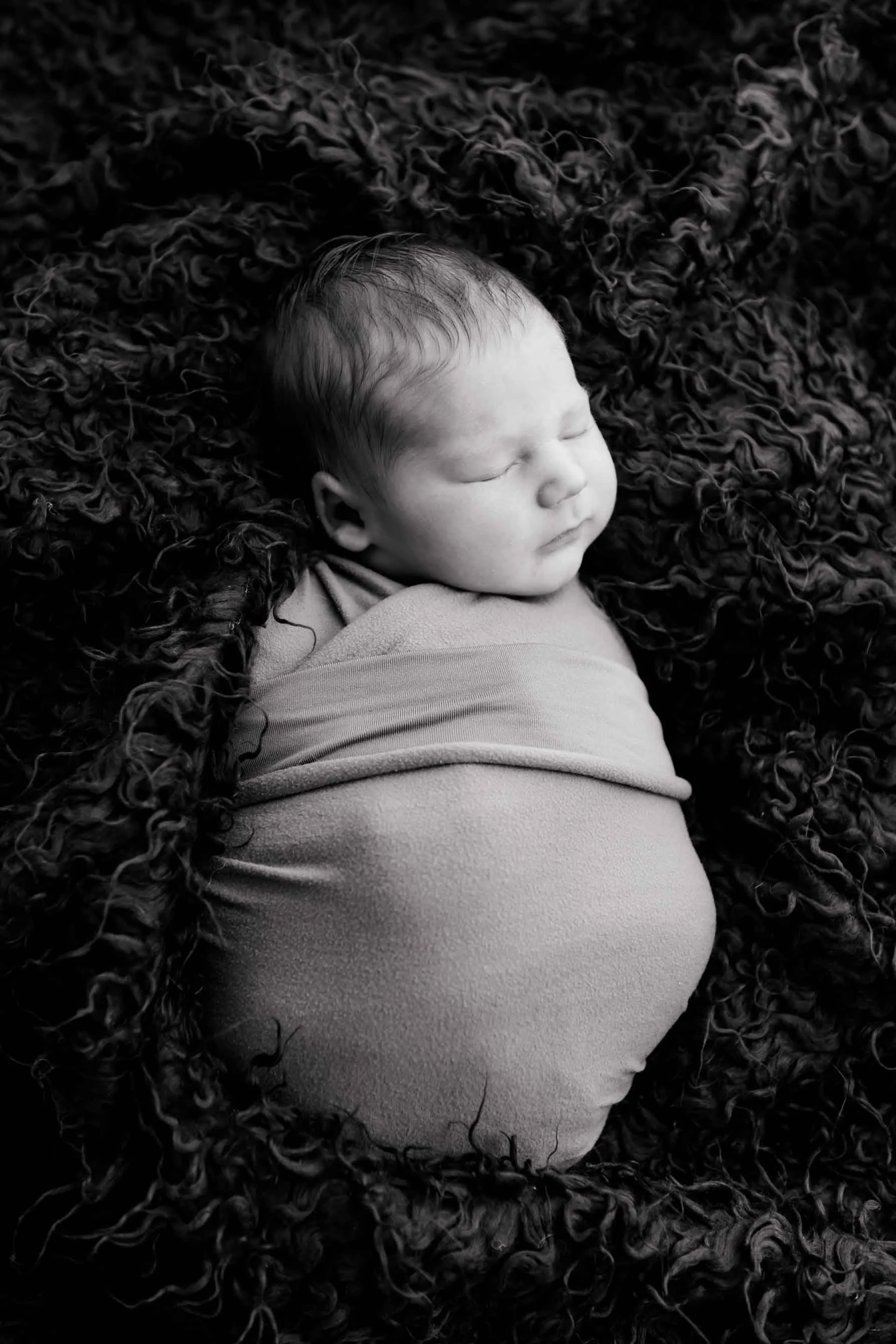 Schwarz-Weiss-Foto eines schlafenden Babys, eingewickelt in eine Decke, auf einem kuscheligen.