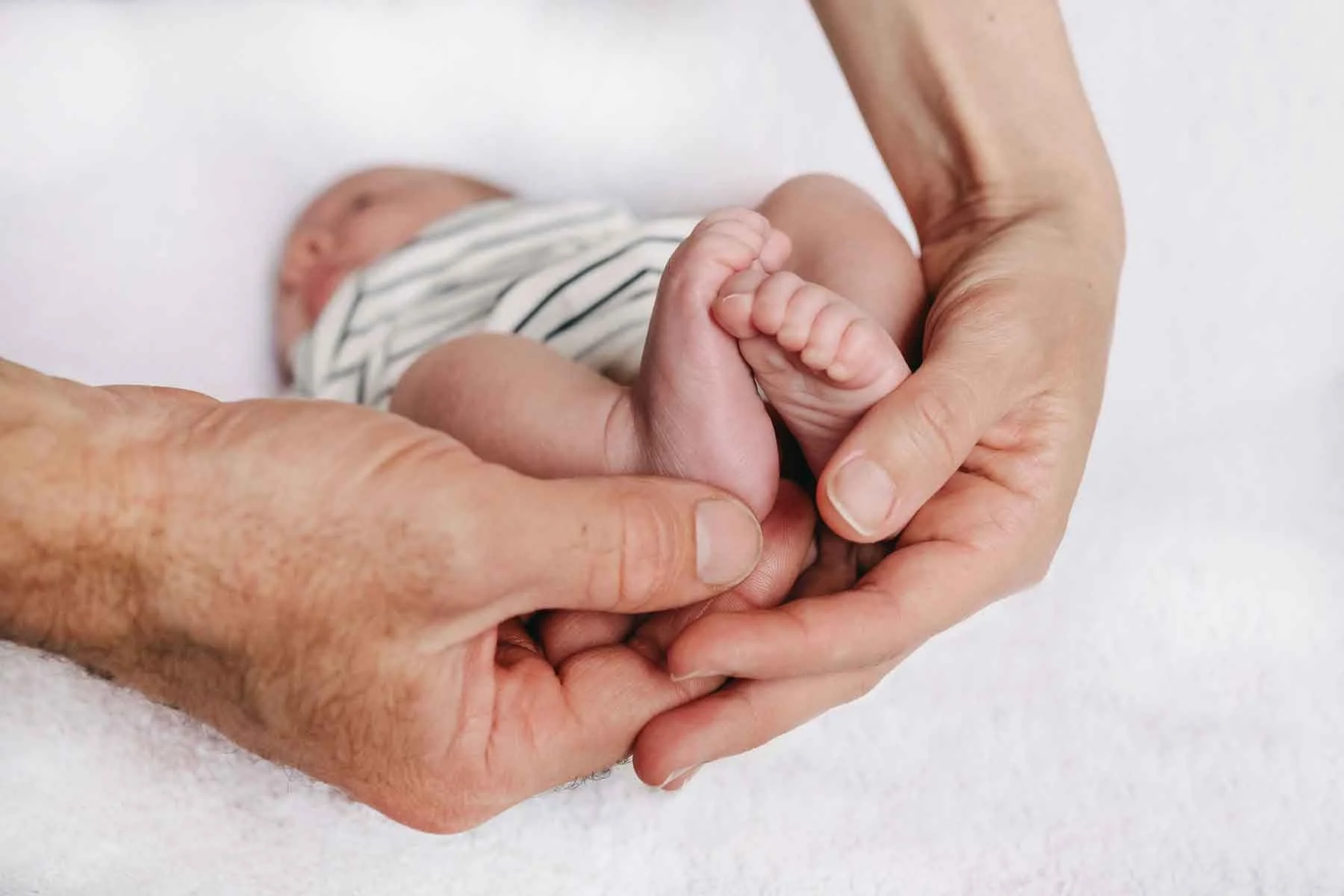Zwei Hände, die Babyfüsse halten, vor einem weissen Hintergrund.