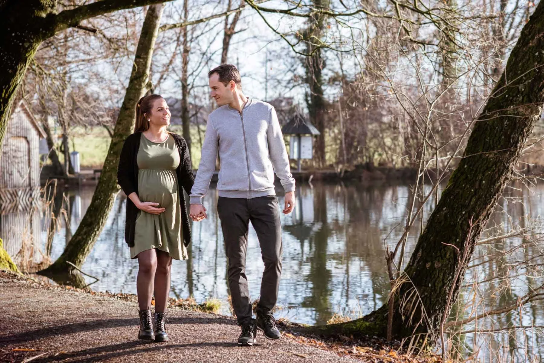 Schwangere Frau trägt einen grünen Rock und ein schwarzes Oberteil, der Mann trägt eine graue Jacke und schwarze Hosen.