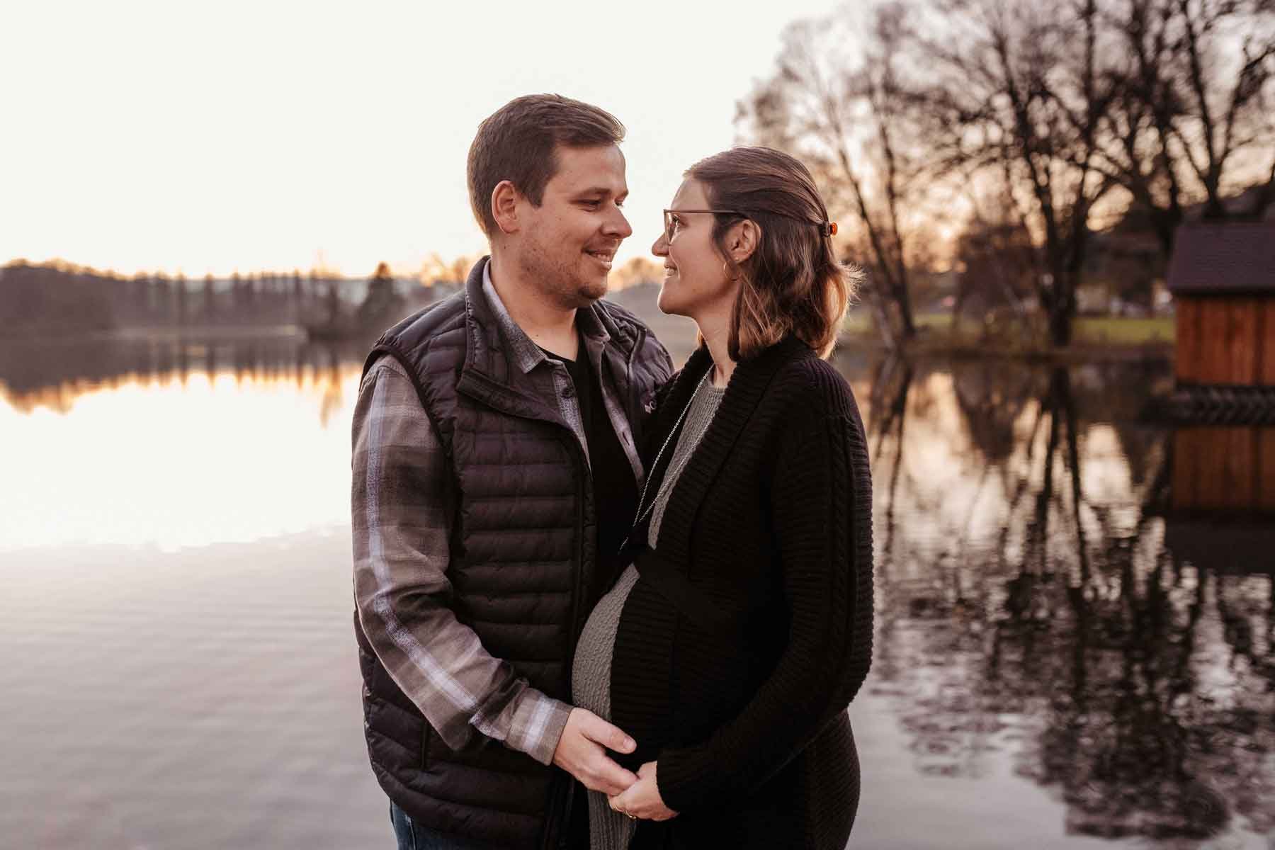Schwangere Frau mit Mann am Weiher bei Sonnenuntergang.