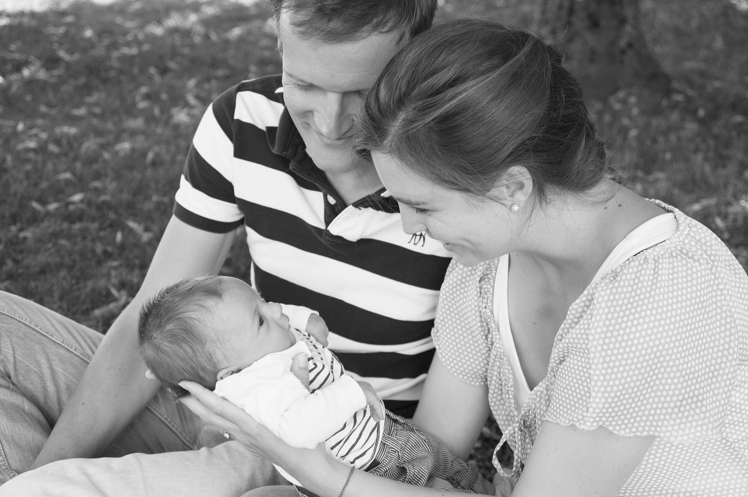 Die Eltern halten ihr Baby im Freien, schwarz-weiss Foto, beide Eltern schauen das Baby liebevoll an.
