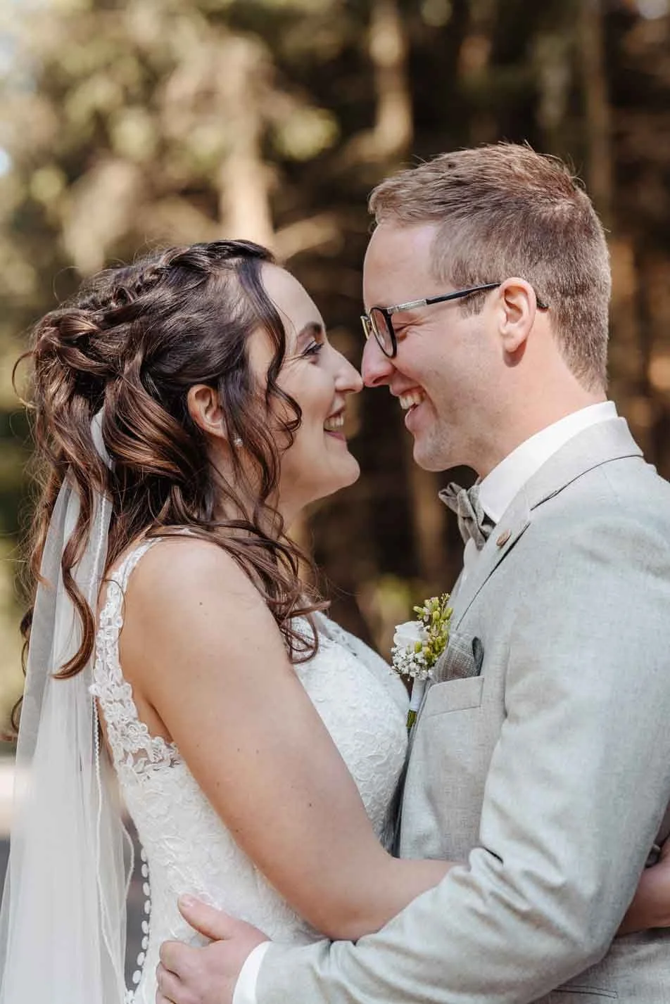 Ein verliebtes Brautpaar bei ihrer Hochzeit, die sich gegenüberstehen, lachen und sich tief in die Augen schauen, im Freien mit Baumhintergrund.