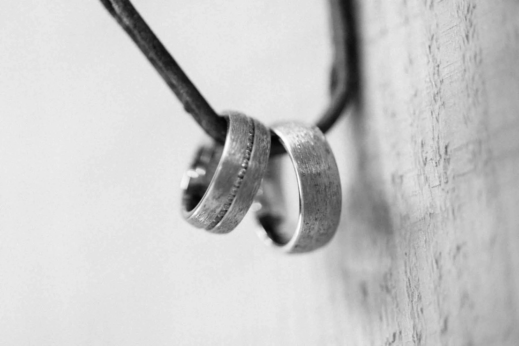 Nahaufnahme von zwei Eheringen, die an einer Wand hängen, in Schwarz-Weiss gehalten.