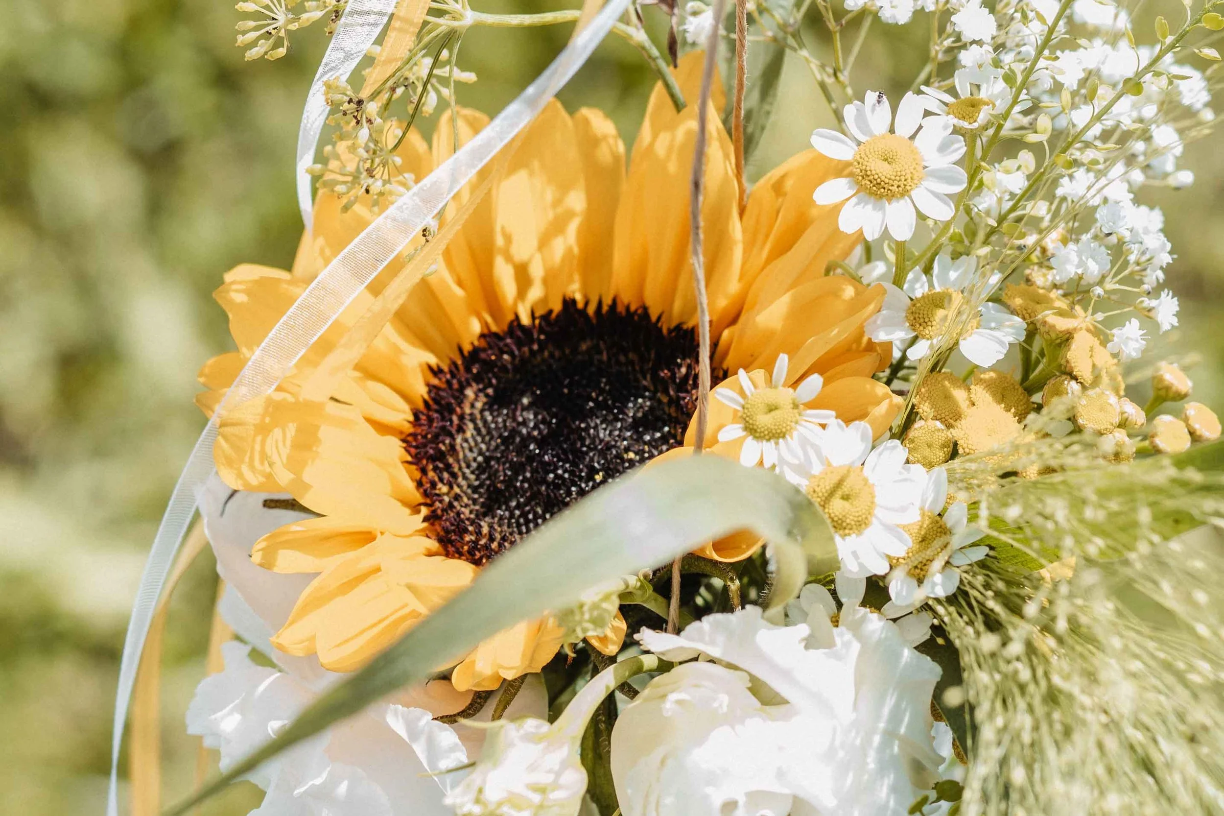 Blumendeko mit Sonnenblume, Gänseblümchen, kleinen weissen Blumen und Gras