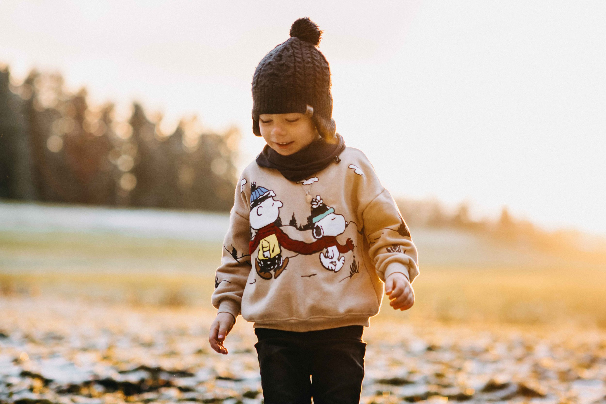 Kind in warmer Kleidung mit Mütze und Pullover, Herbstlandschaft im Hintergrund. Sunset-Stimmung im Winter.