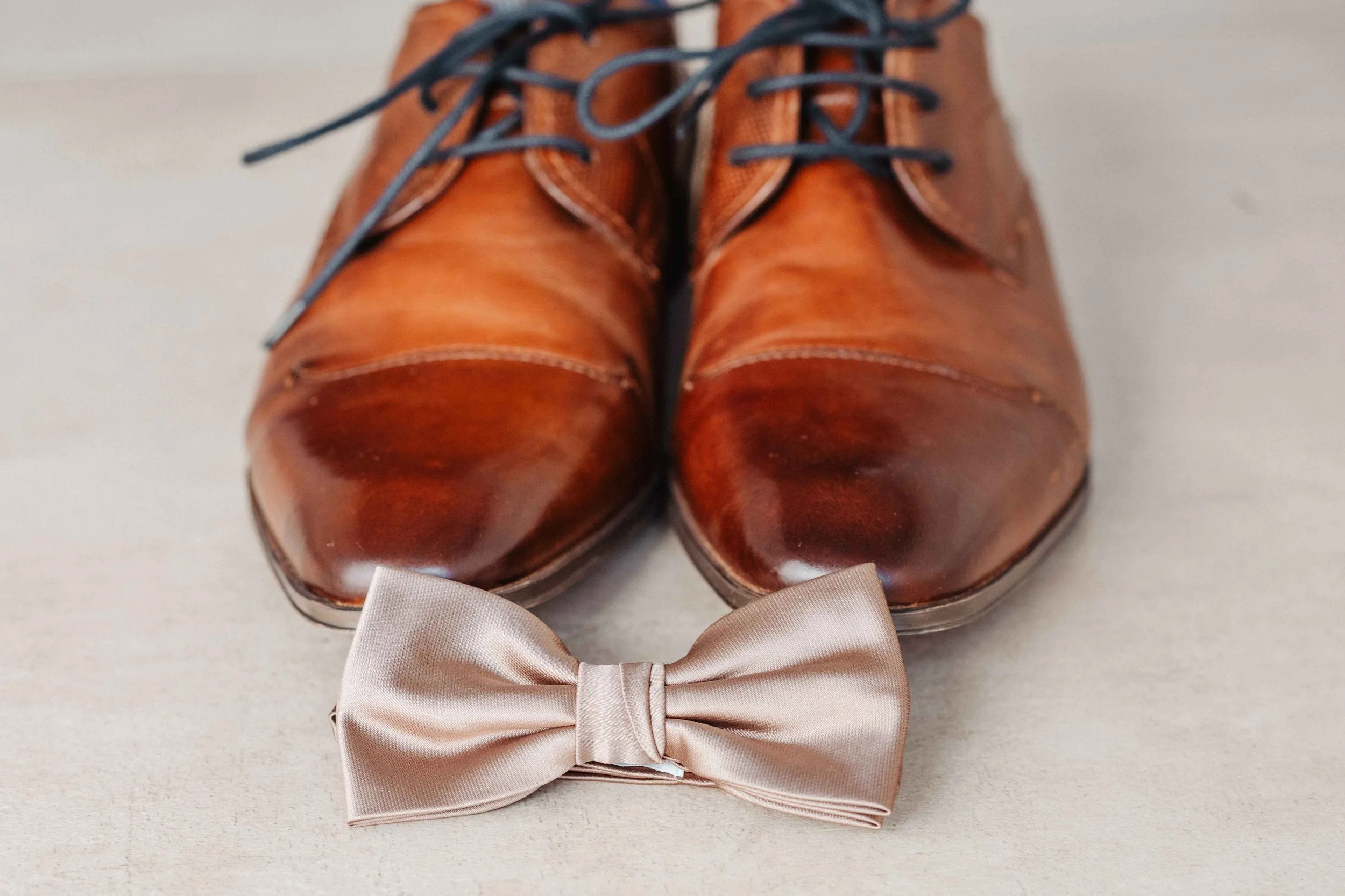 Braune Leder Schuhe mit blauen Schnürsenkeln und ein beige Seidenfliege.