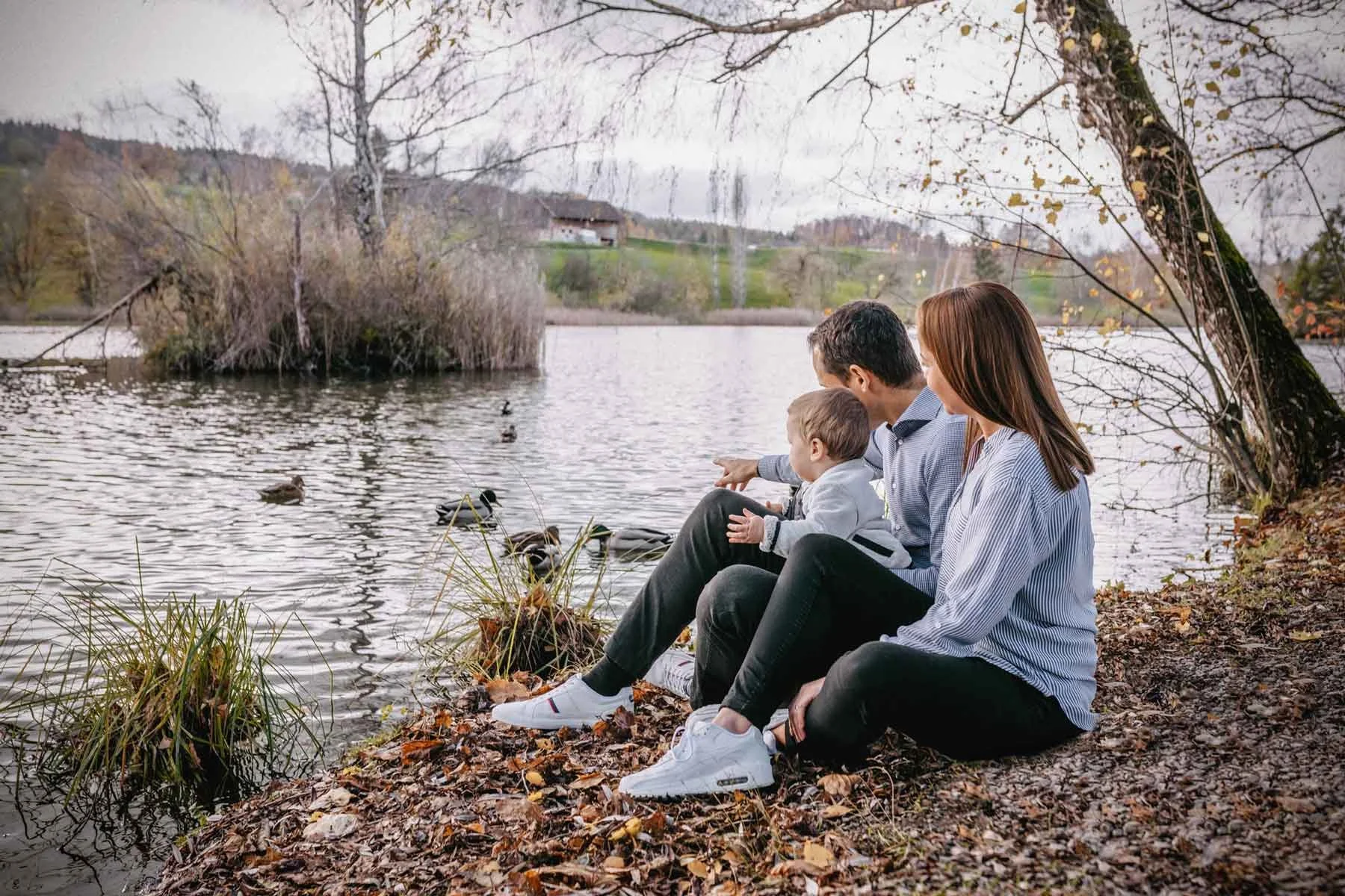 Familie sitzt am Ufer eines Sees und füttert Enten im Herbst