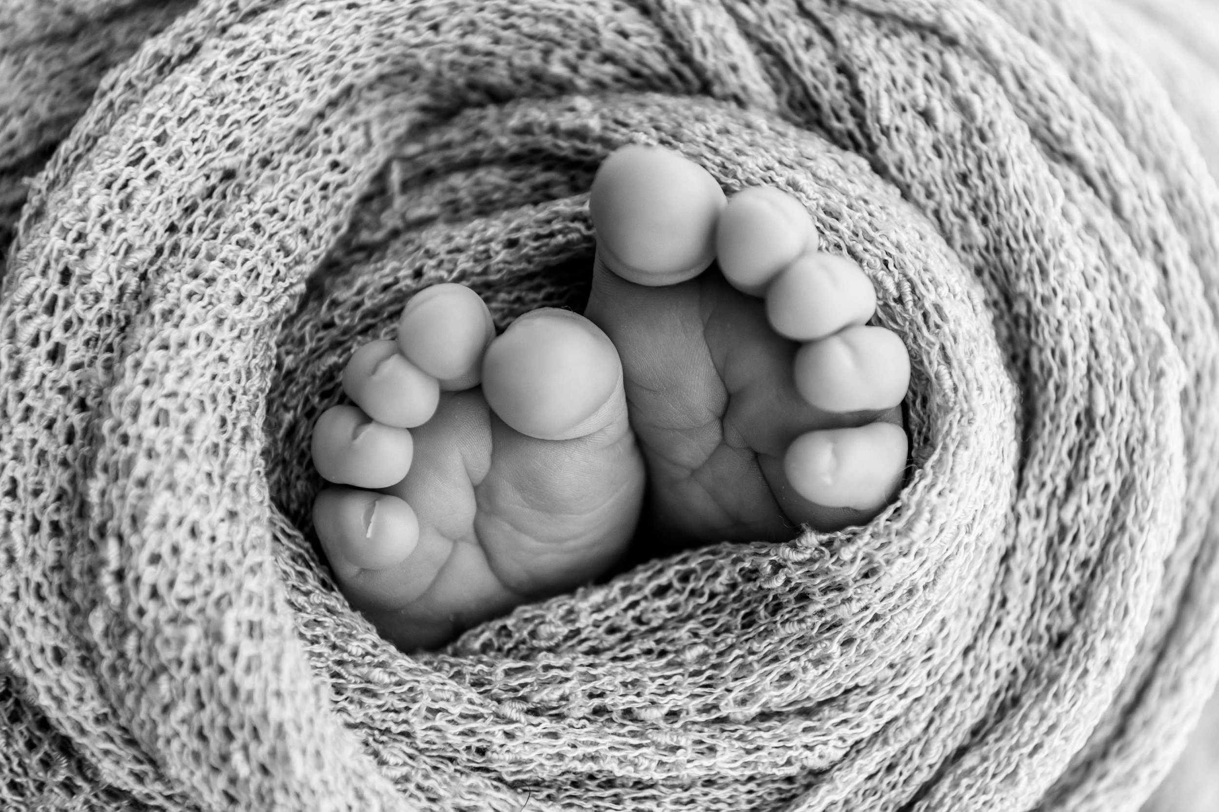 Schwarz-Weiss-Foto von Babyfüßen, die in eine gestrickte Decke gewickelt sind.