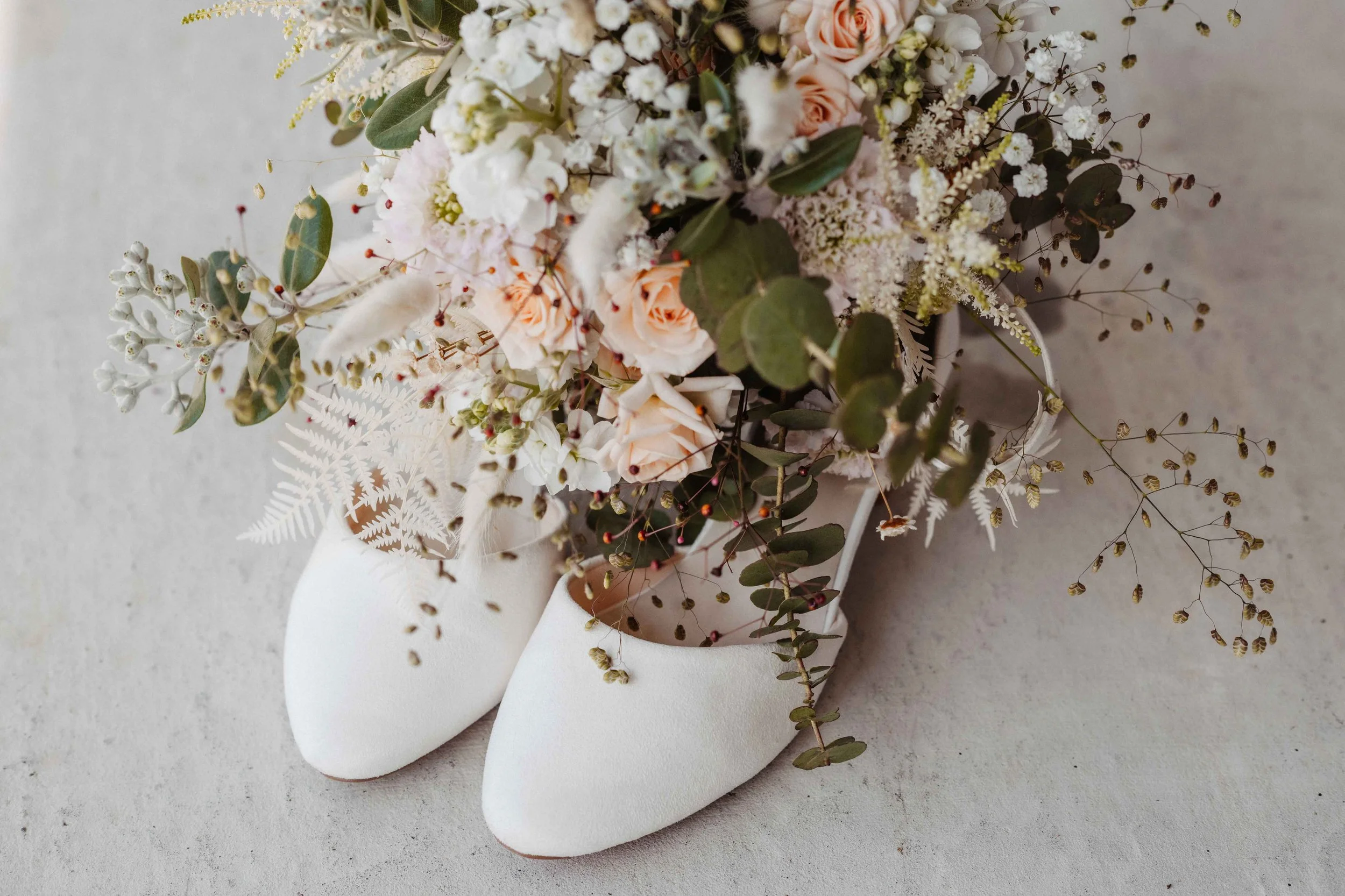 Brautstrauss in weissen Schuhen auf einem Beton Boden.