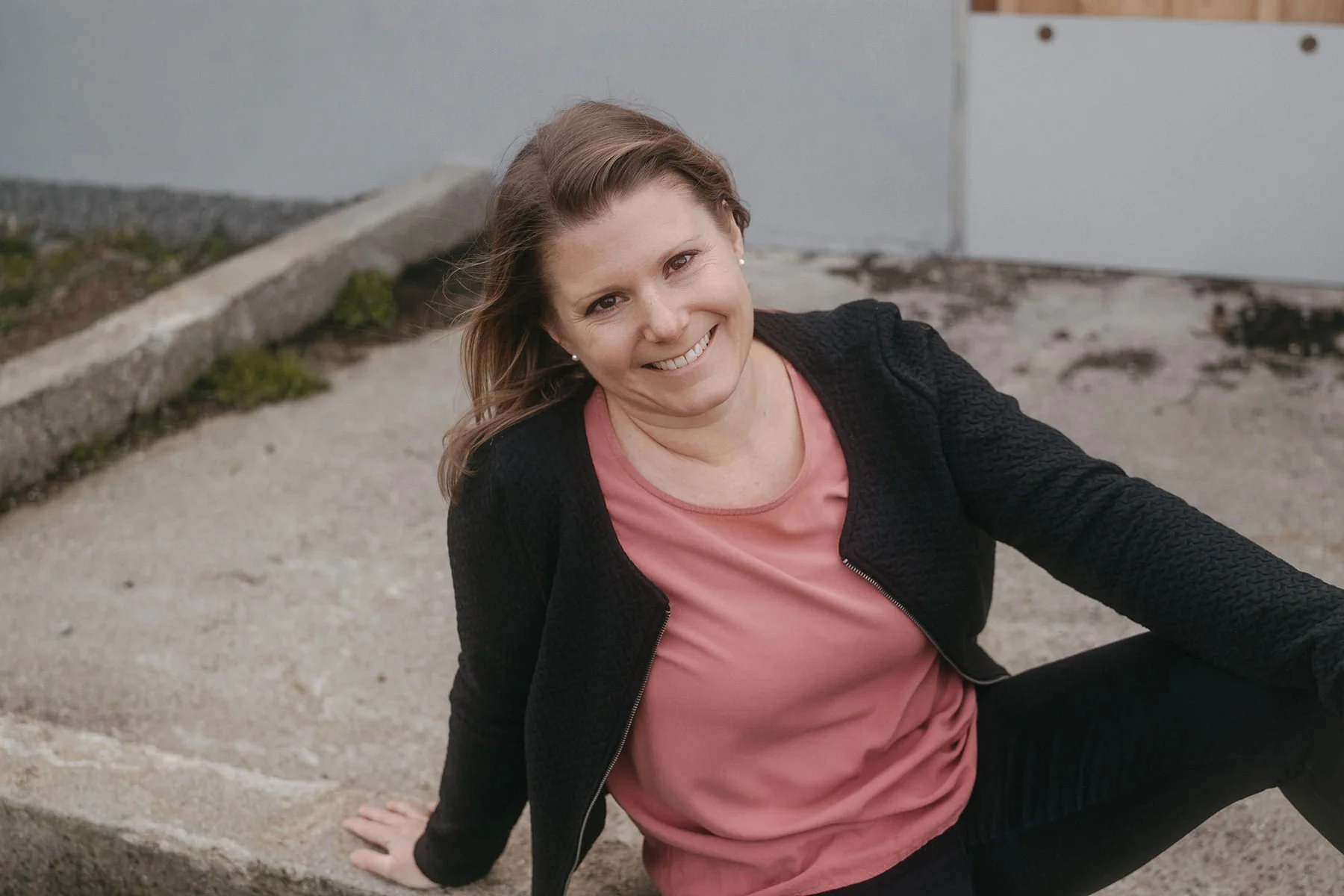 Janine Huber lächelnd sitzt draussen auf Betonboden.