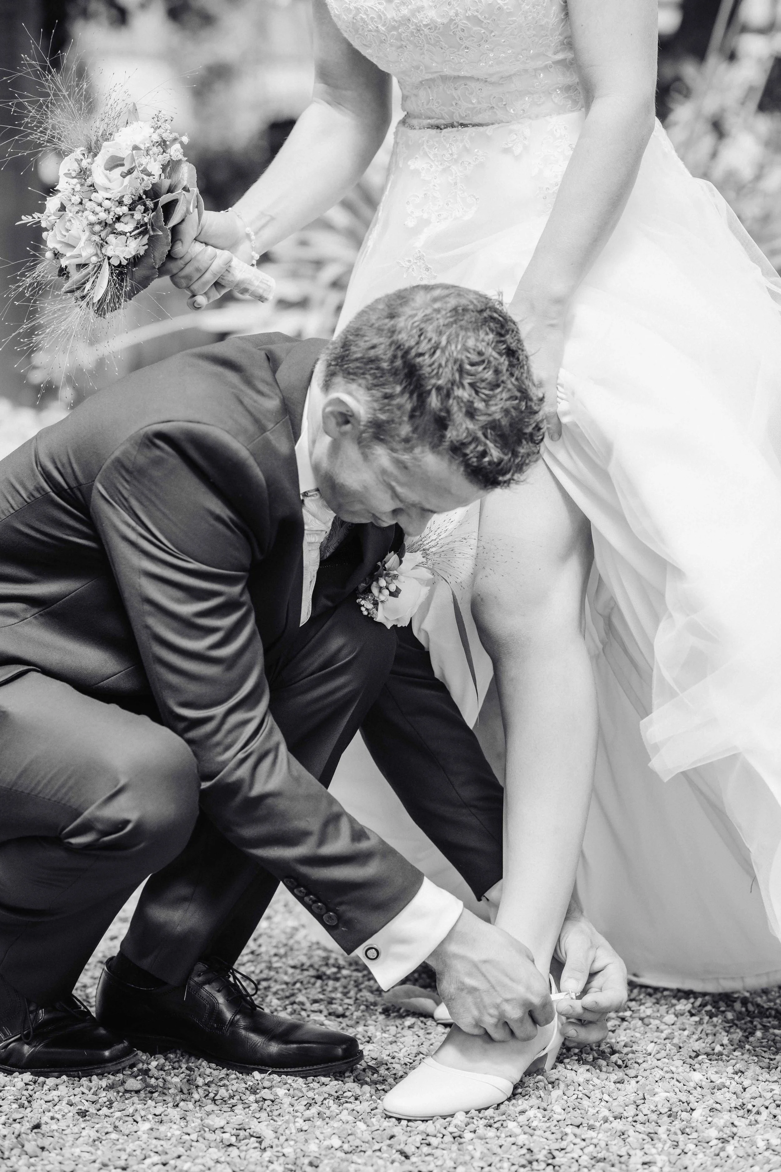 Ein Mann hilft einer Braut, ihre Schuhe zu binden bei einer Hochzeit.