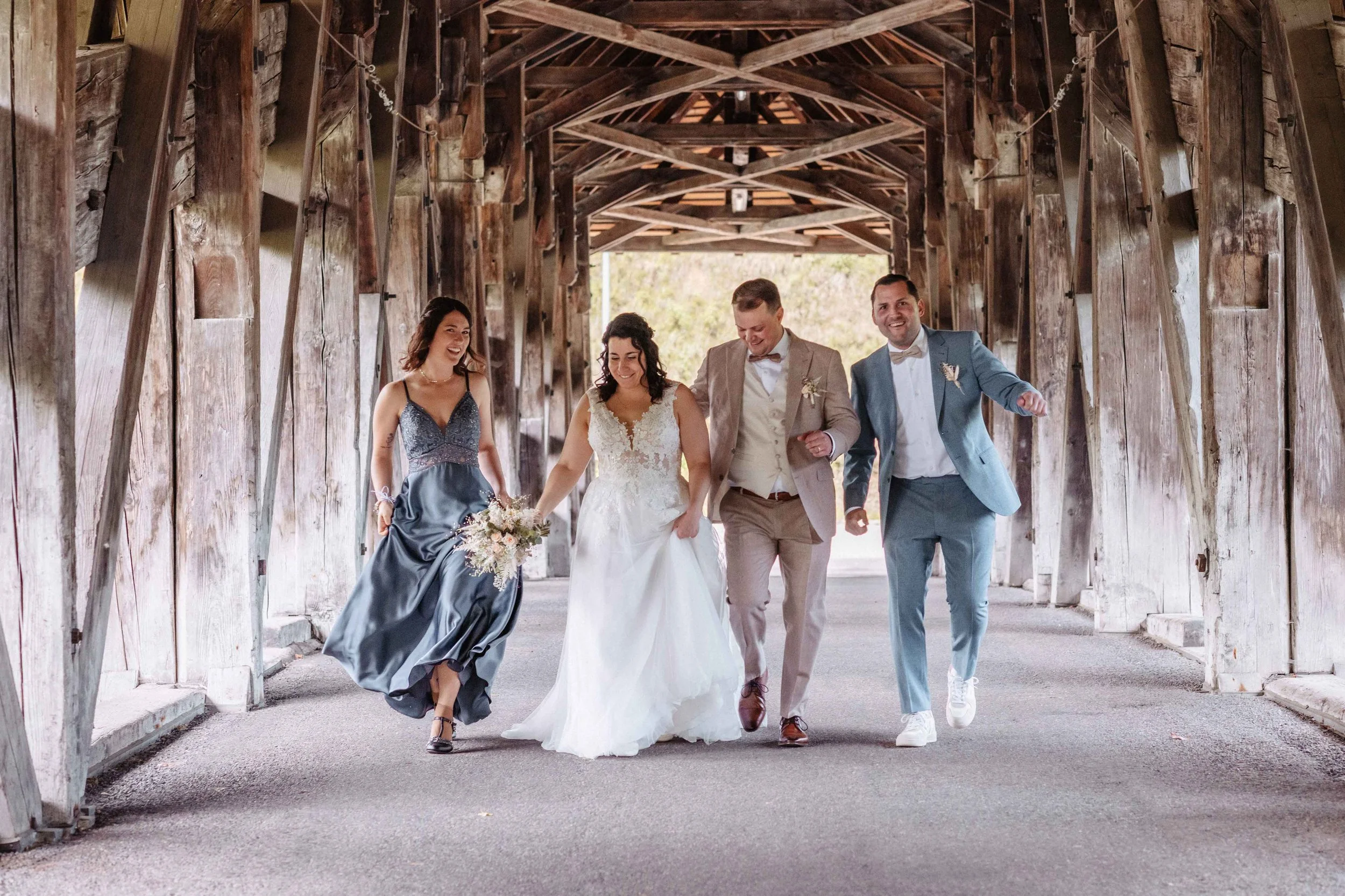 Brautpaar mit Trauzeugen laufen auf der alten Holzbrücke tanzend, lachend und freuen sich.
