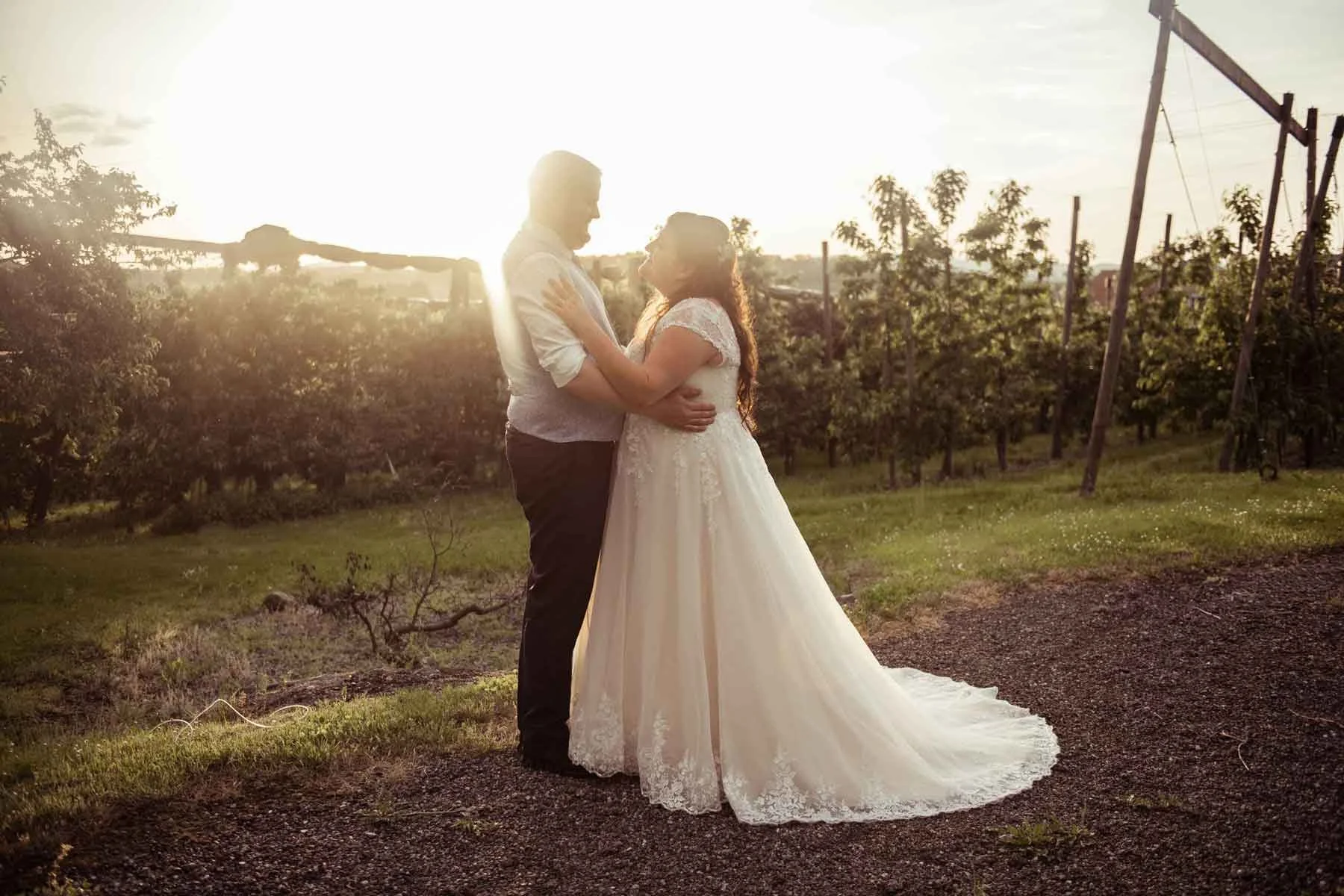 Ein Brautpaar auf einer Wiese bei Sonnenuntergang, die sich umarmend, mit einem Weinberg im Hintergrund.