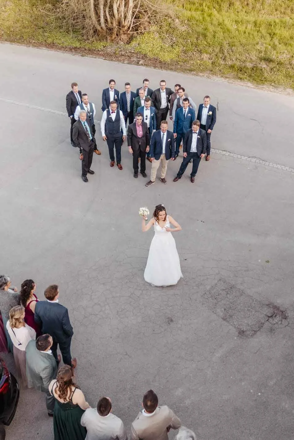 Braut steht im Mittelpunkt, von einer Gruppe von Männern in Anzügen umgeben um den Brautstrauss zu werfen.