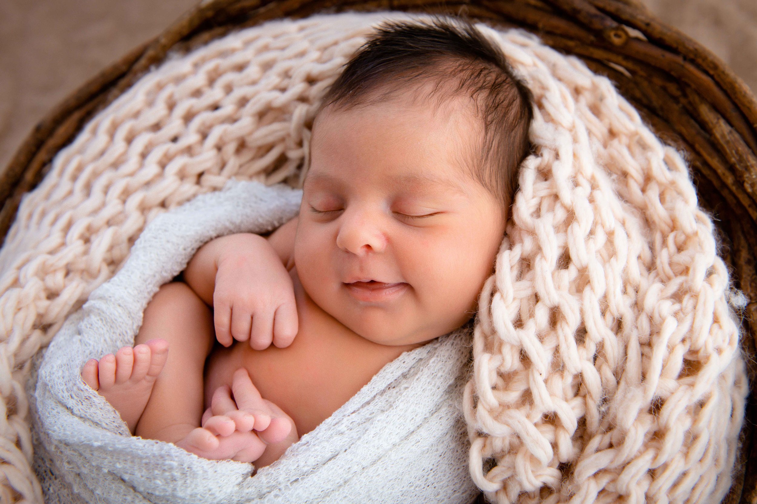 Schlafendes Baby in einem gestrickten, beigen Tuch gewickelt.