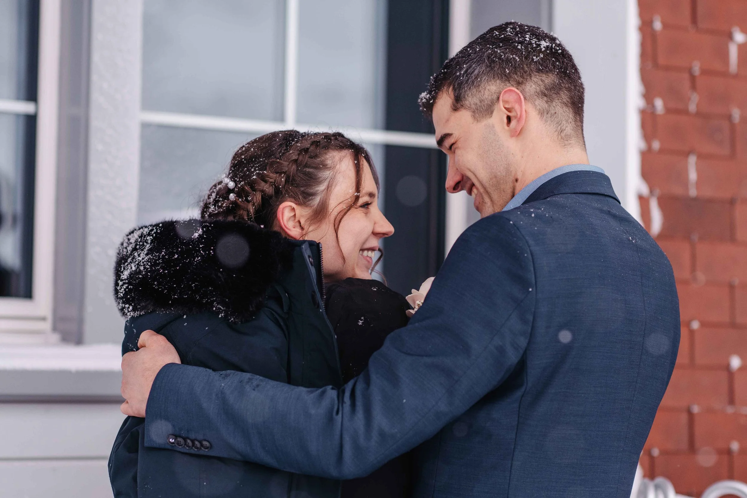 Ein verliebtes Brautpaar umarmt sich draussen im Schnee, beide lachen glücklich.