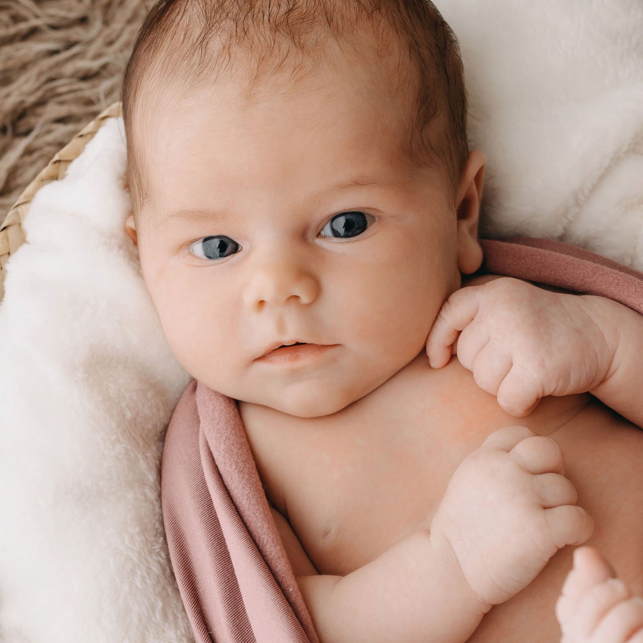 Nahaufnahme eines Babys, das auf einer weichen Decke liegt und in ein rosafarbenes Tuch gewickelt ist.