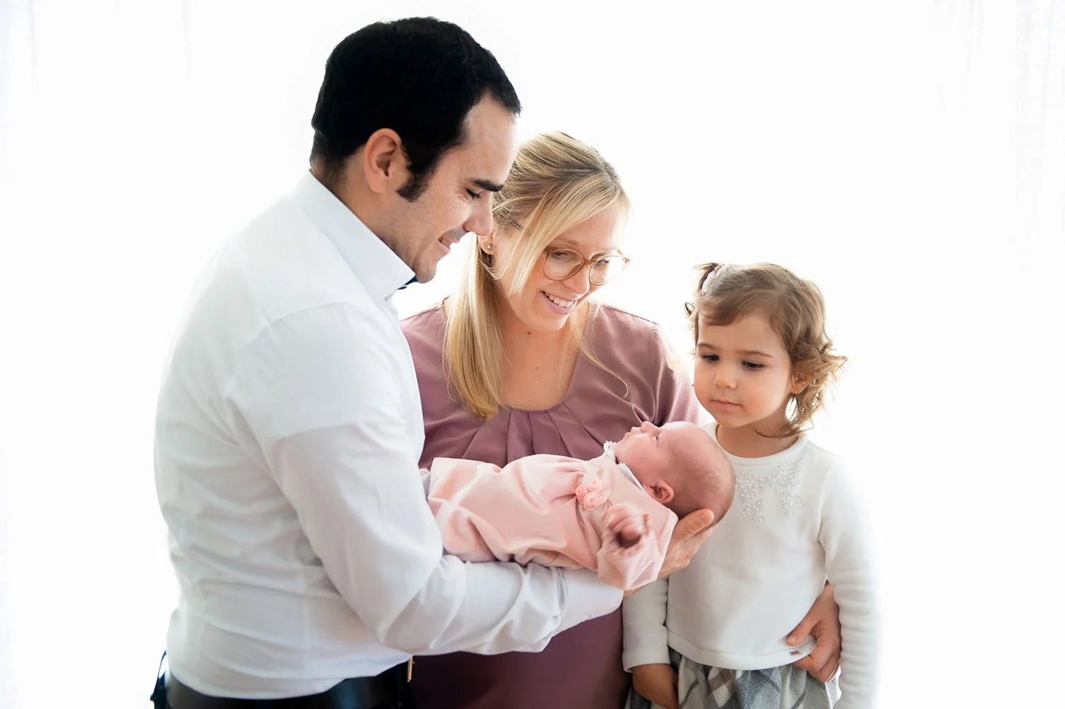 Familie mit zwei Erwachsenen, einem Baby und einem kleinen Mädchen. Sie sind in einem hellen Raum.