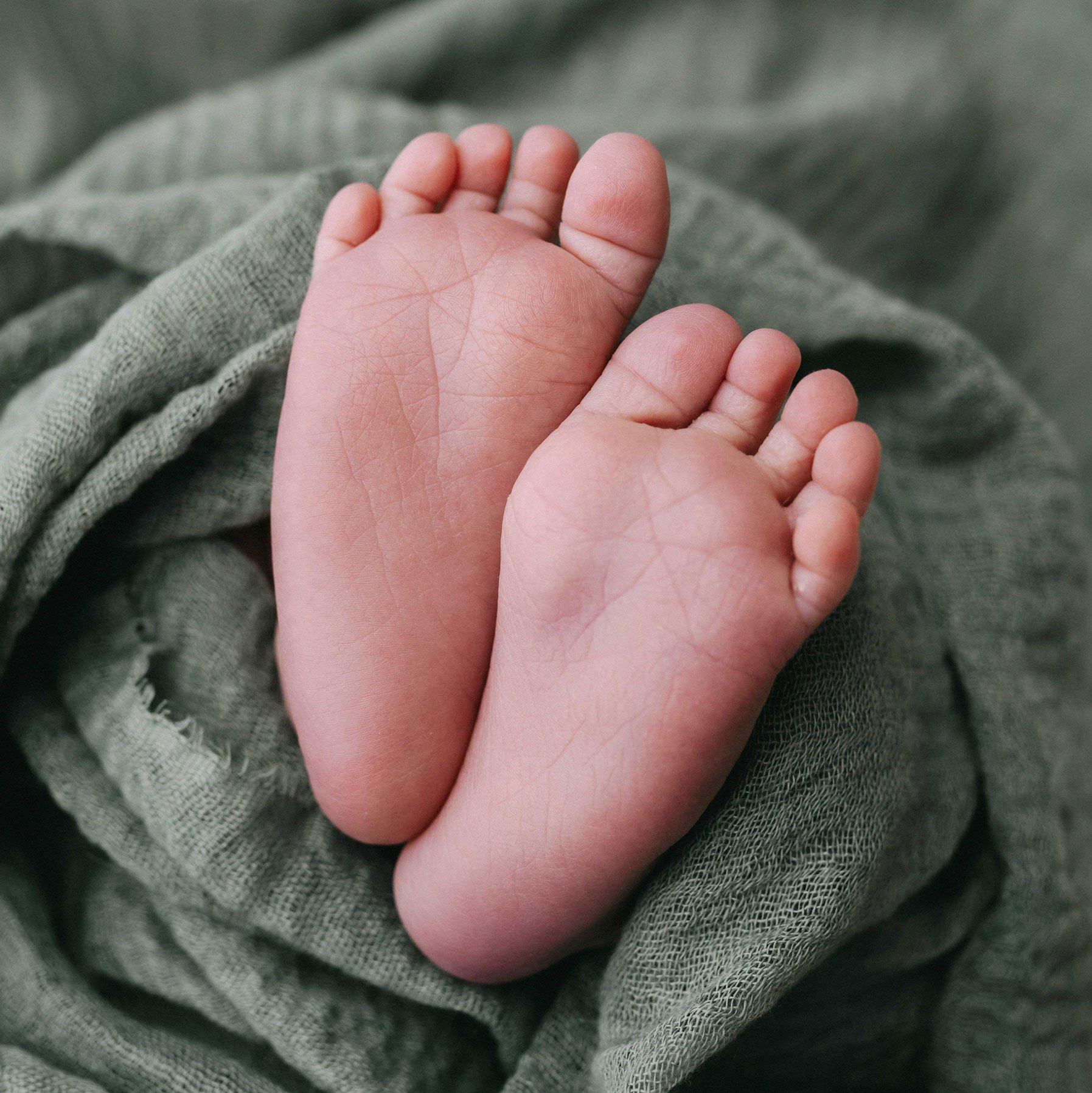Nahaufnahme von Babyfüssen auf einem grünen Stoffhintergrund.