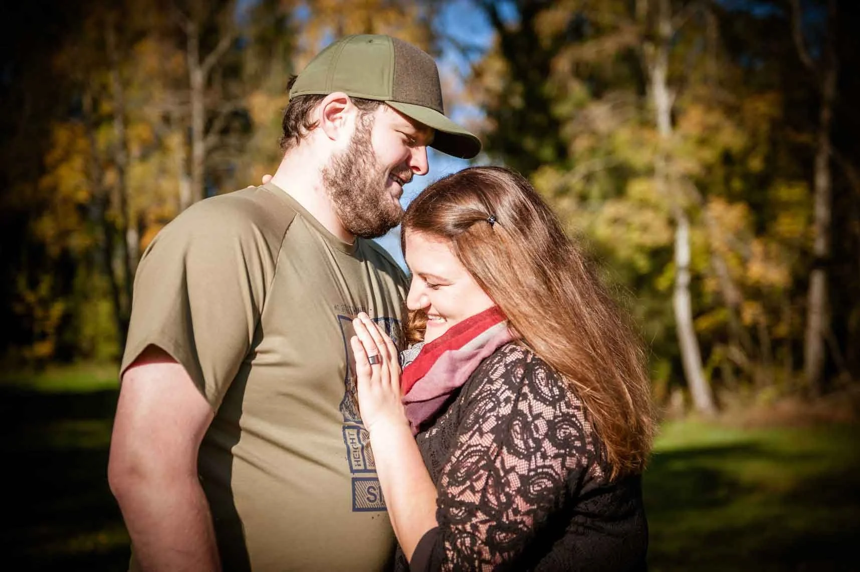 Ein lachendes Paar steht sich im Freien gegenüber, umgeben von Bäumen mit herbstlicher Laubfärbung, bei Sonnenschein.