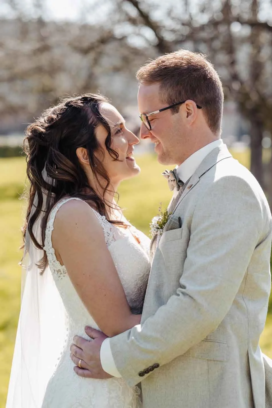 Braut trägt ein weisses Hochzeitskleid und der Bräutigam einen hellgrauen Anzug, sie schauen sich liebevoll in die Augen.