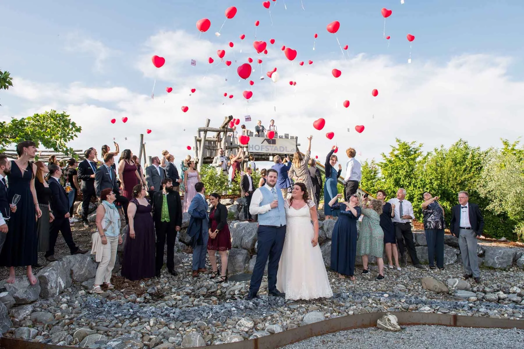 Hochzeit mit vielen Gästen, die rote Herzluftballons steigen lassen.