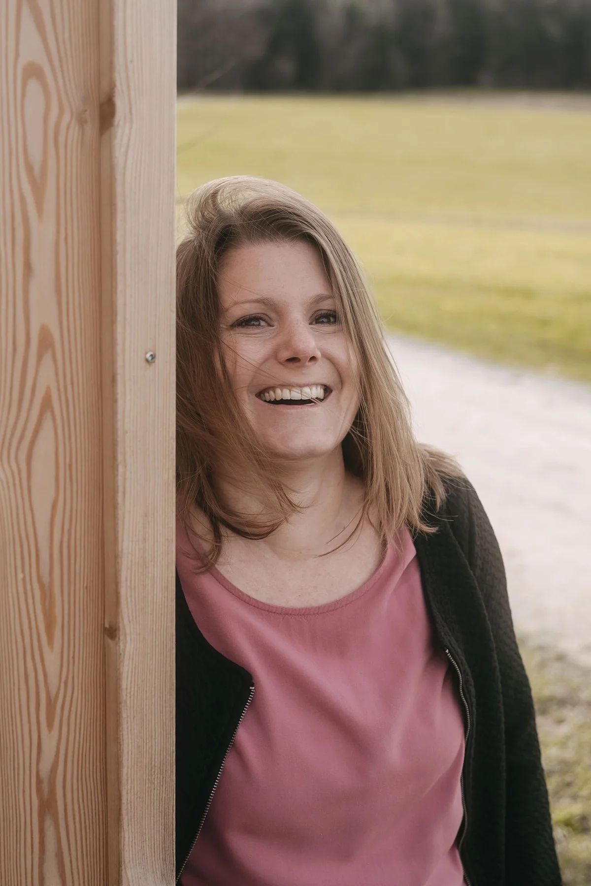 Lachend steht Janine Huber draussen neben einer Holzwand.