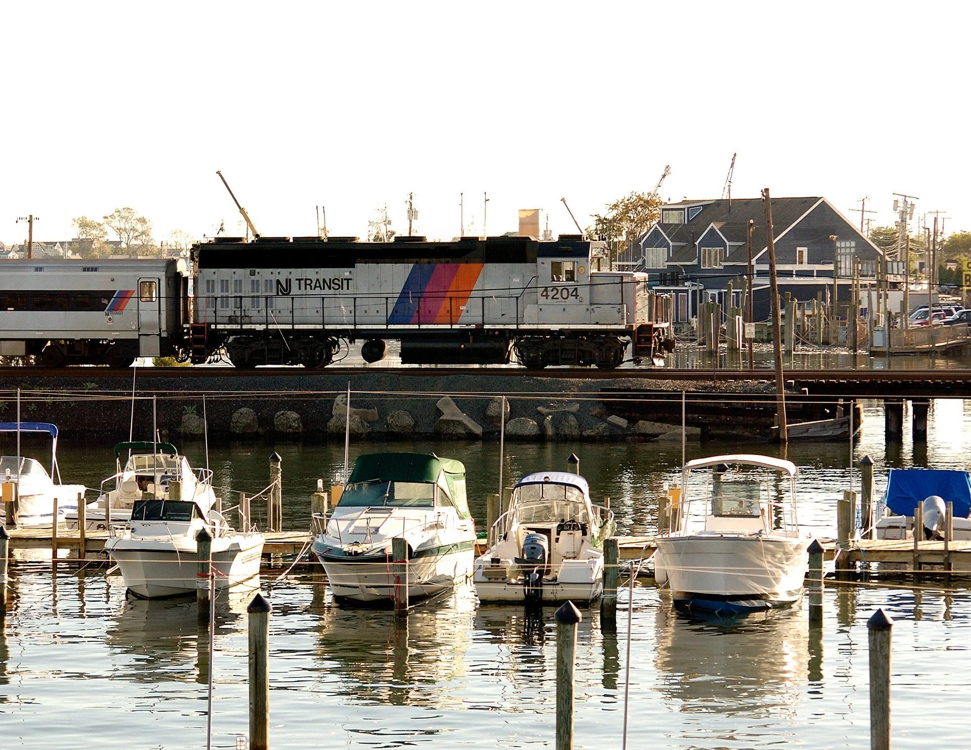 New Jersey Transit train riding on a track over water with boats in the foreground