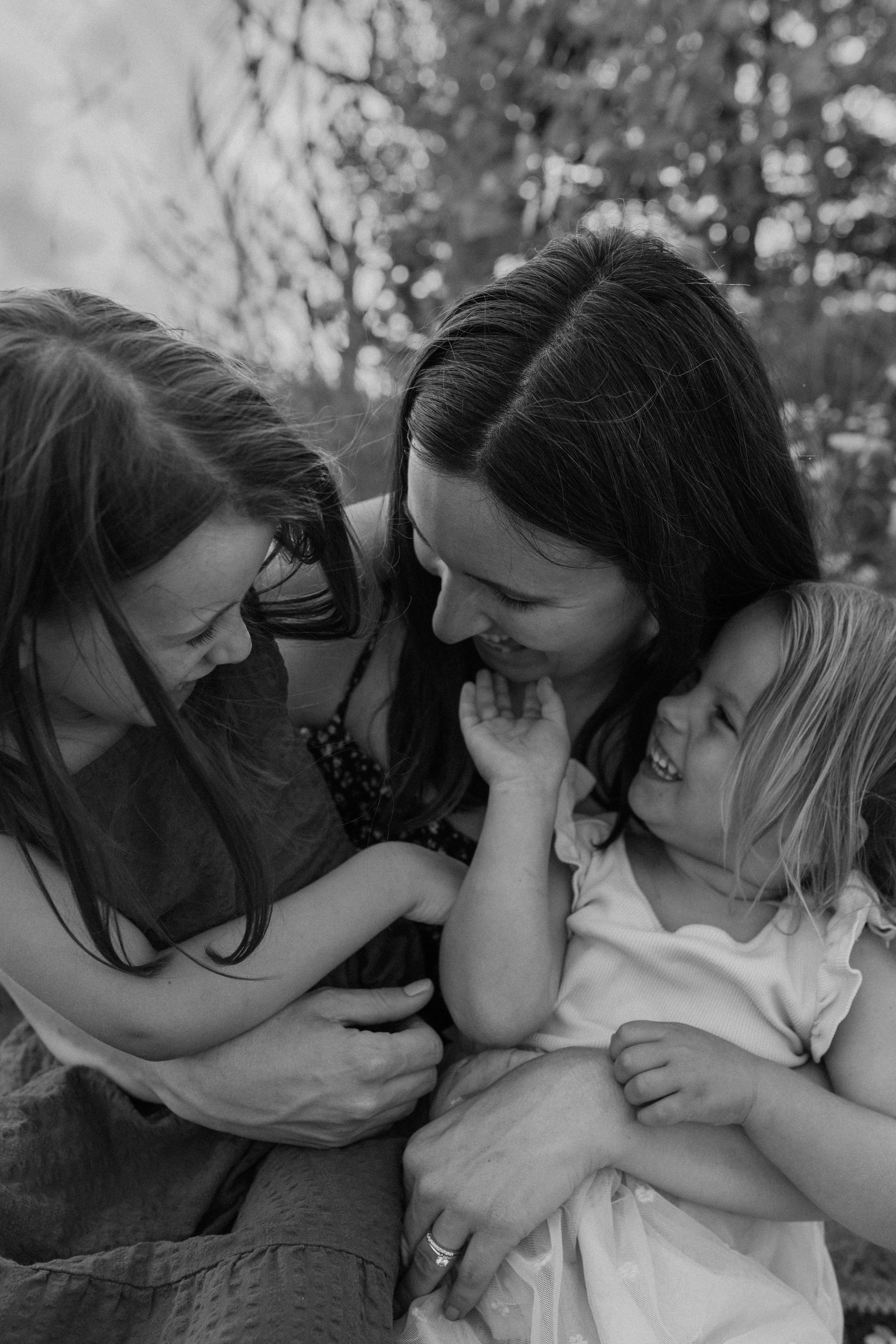 A black and white photo of a mom and her two young daughters tickling each other and laughing, during their family photo session in the Durham Region