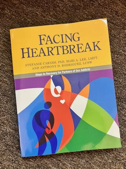 Book titled "Facing Heartbreak" about recovery for partners of sex addicts, featuring colorful abstract human figures on the cover.