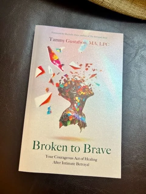 A book titled "Broken to Brave" by Tammy Gustafson, MA, LPC, resting on a dark surface, with an image of a colorful, shattered glass brain on the cover.