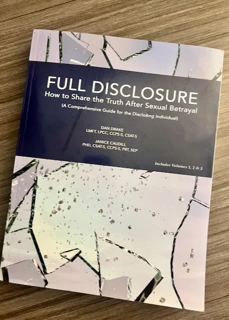 Book titled "Full Disclosure: How to Share the Truth After Sexual Betrayal" laying on a wooden surface. The cover is divided into a dark blue upper section and a white lower section with a cracked glass design.