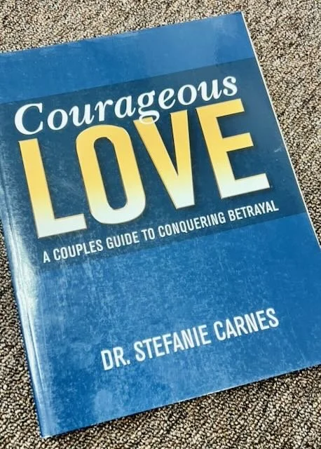 Book titled 'Courageous Love: A Couple's Guide to Conquering Betrayal' by Dr. Stefanie Carnes on a textured surface.