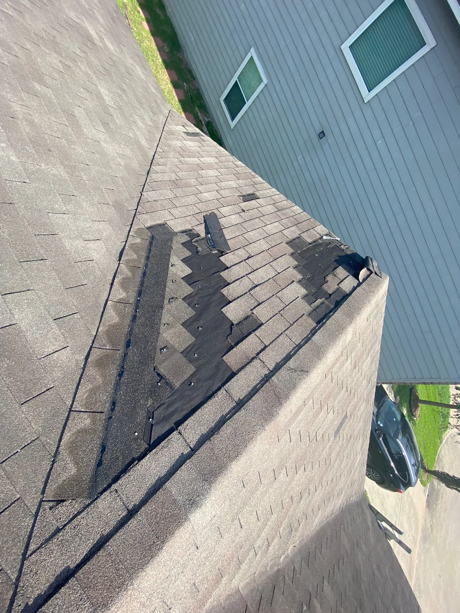 Close-up of a house roof undergoing repair, with shingles lifted and a roofing tool visible.