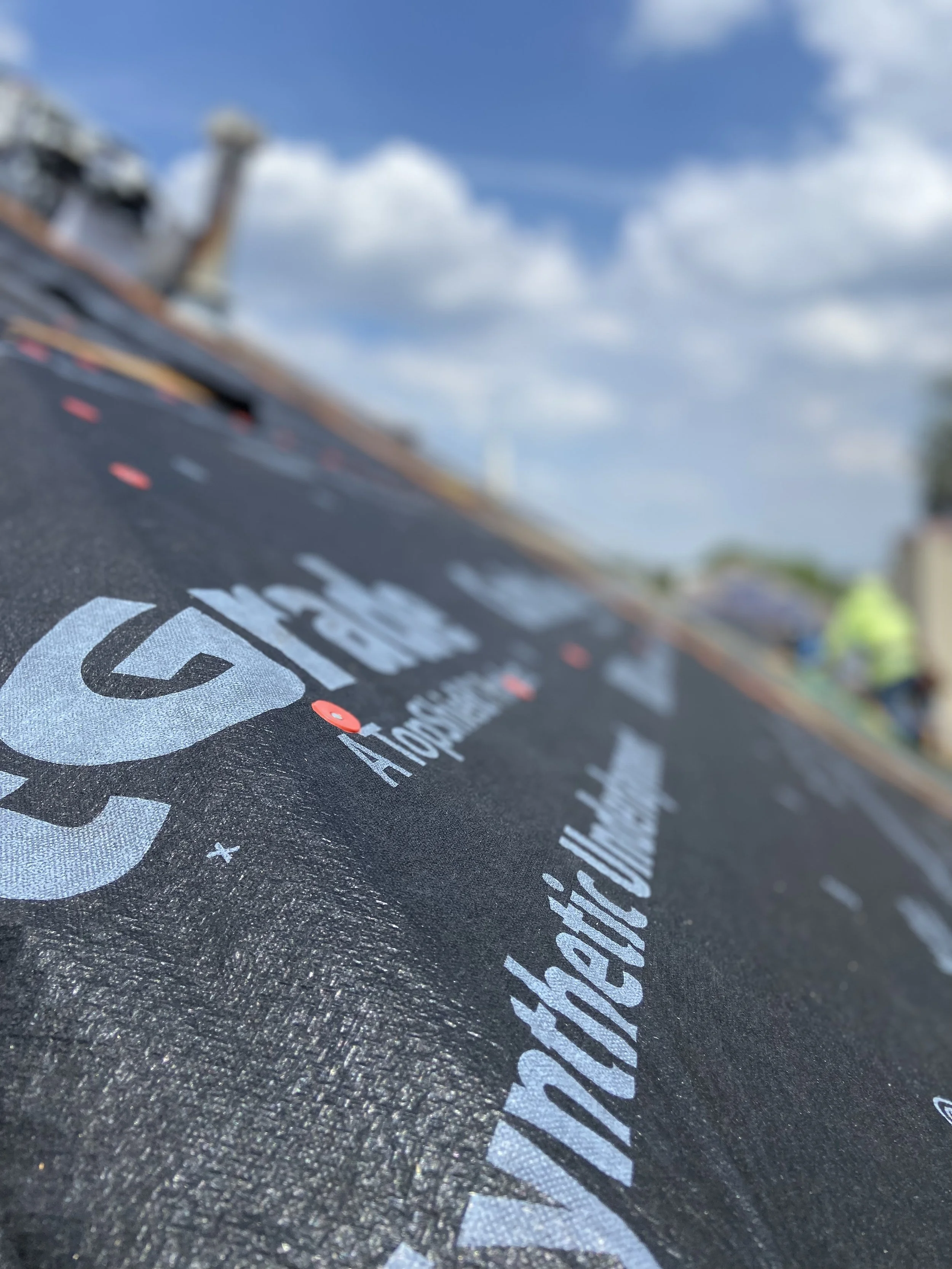 Close-up of a roofing material with printed text, with a partly cloudy sky in the background.