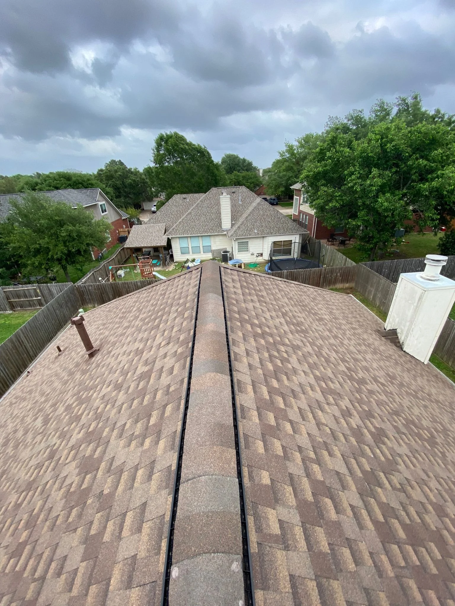 View of rooftops, backyard fences, trees, and neighboring houses under a cloudy sky.