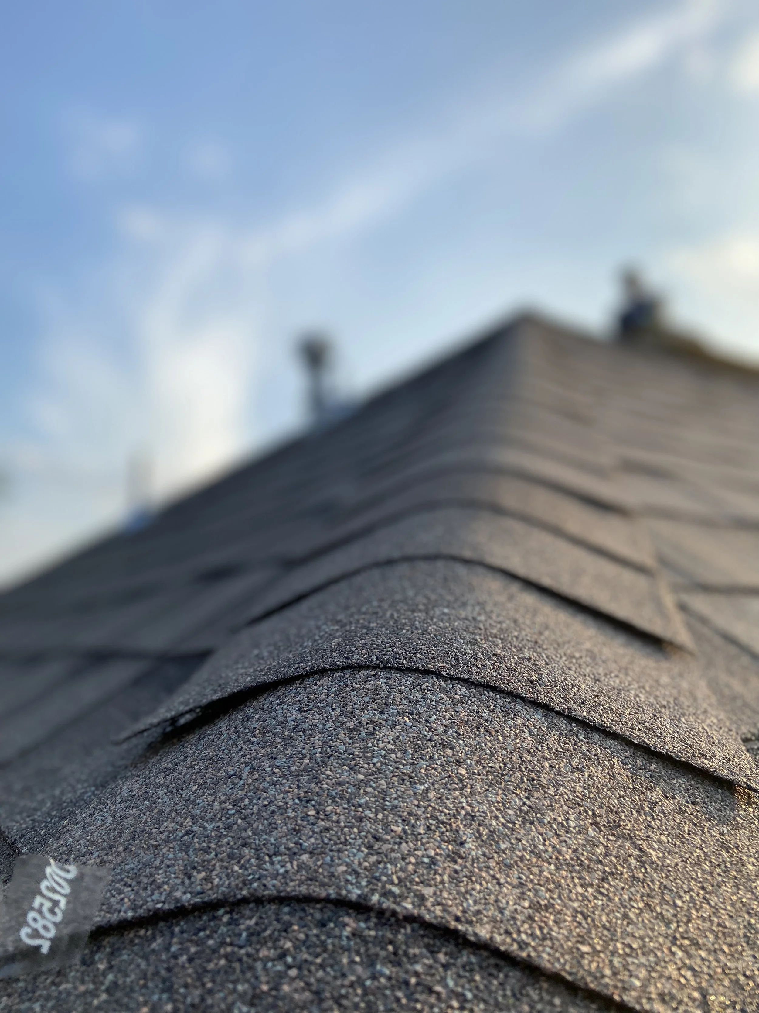 Close-up of a sloped asphalt shingle roof with a clear blue sky in the background.