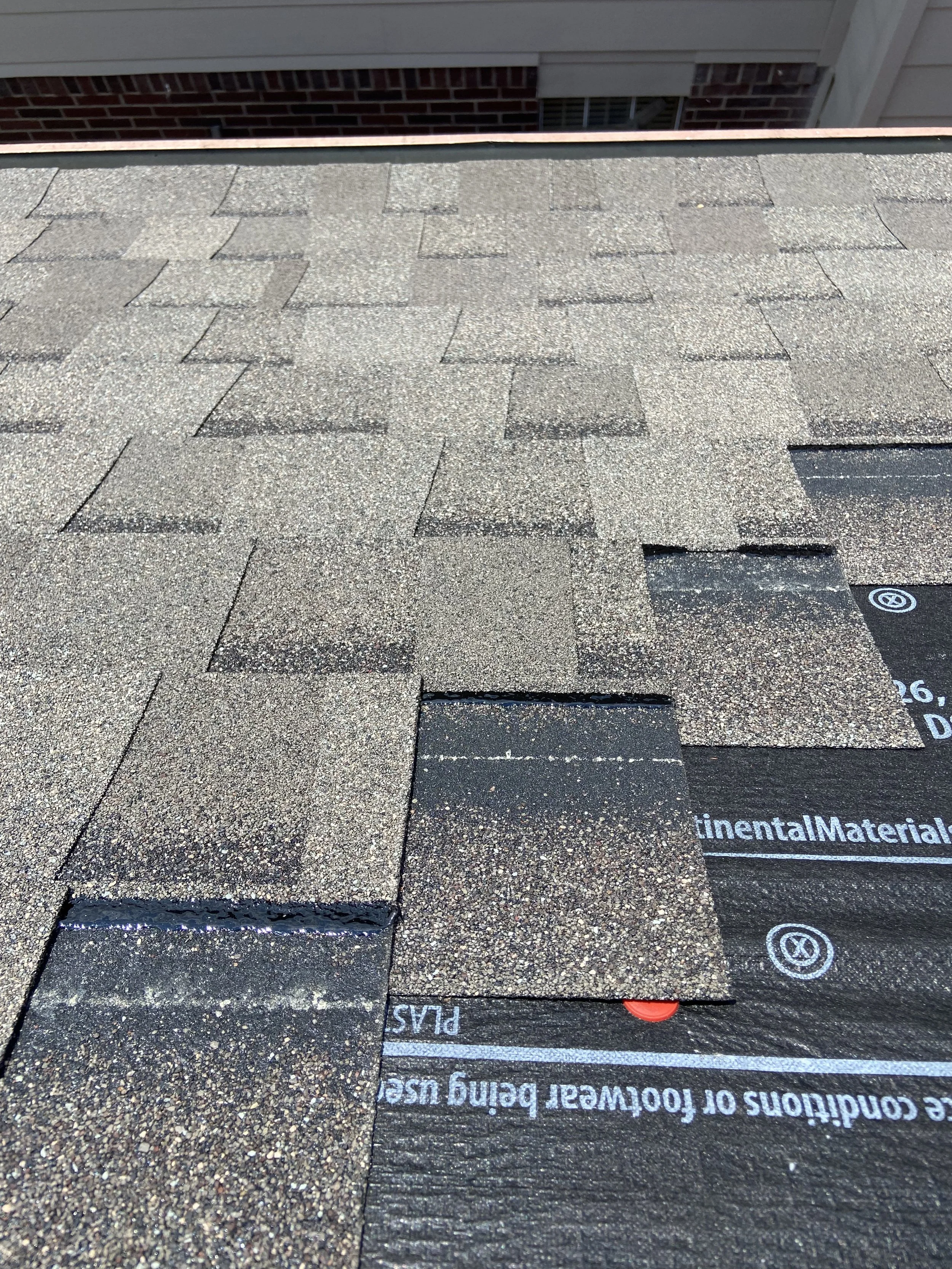 Close-up of a rooftop with asphalt shingles and underlayment material visible in some areas.