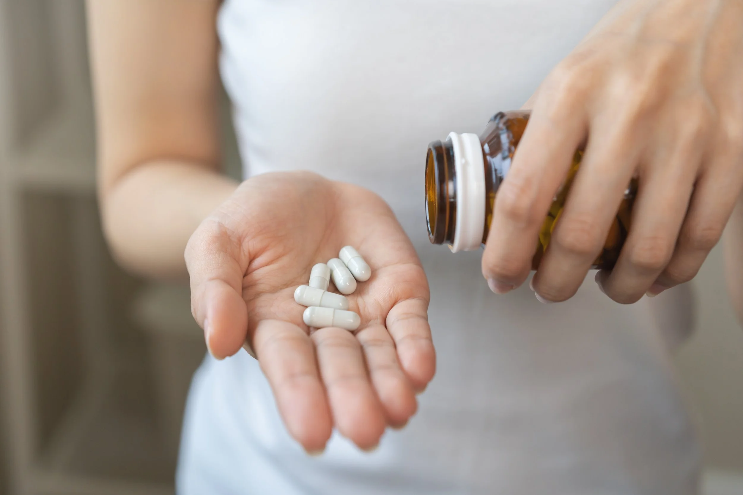 Person pouring pills from a brown bottle into their hand.