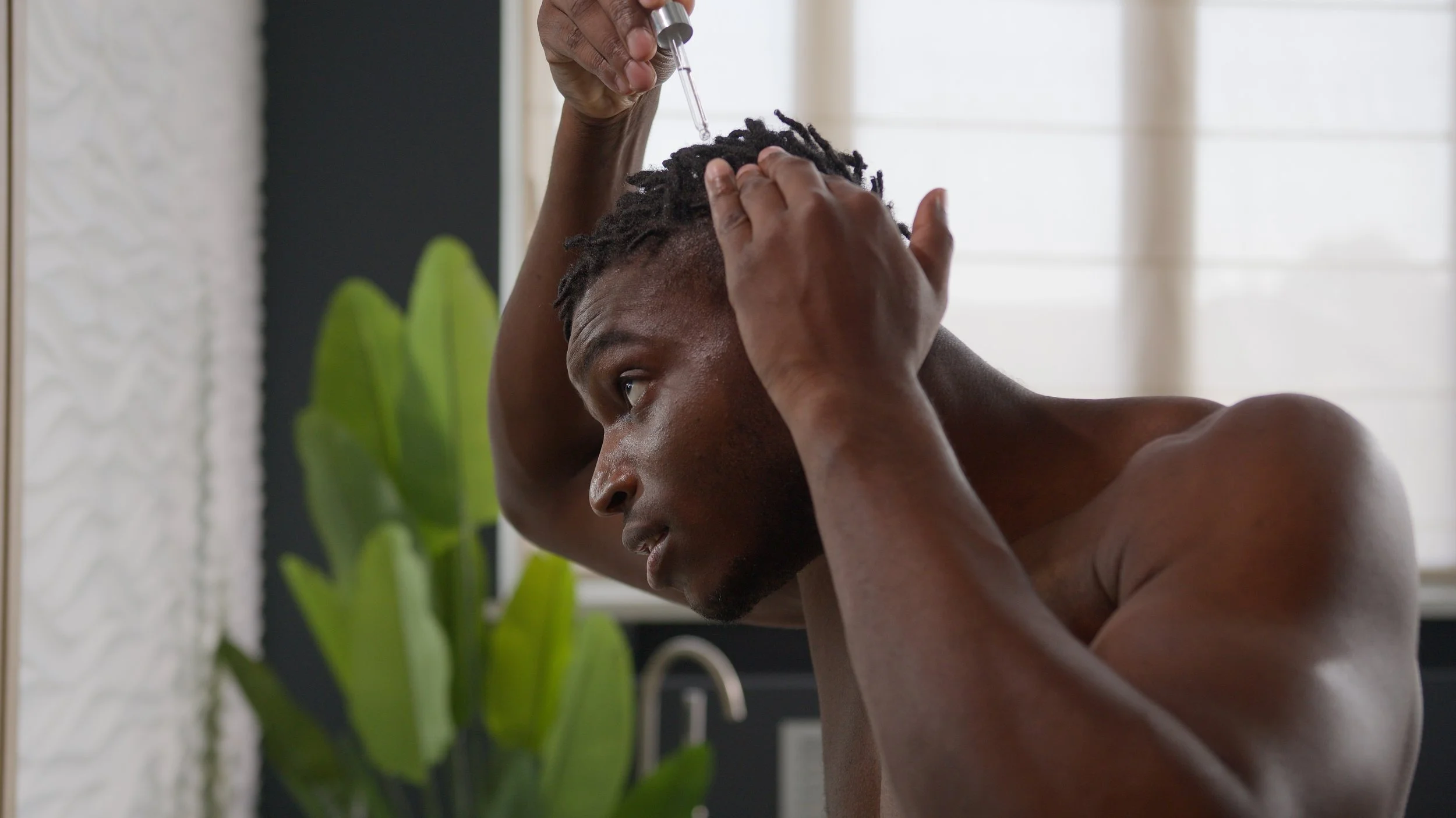 A man applying medication or treatment to his scalp using a dropper.