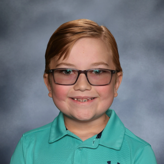 A young boy with short, light brown hair and glasses, smiling, wearing a teal polo shirt against a gray background.