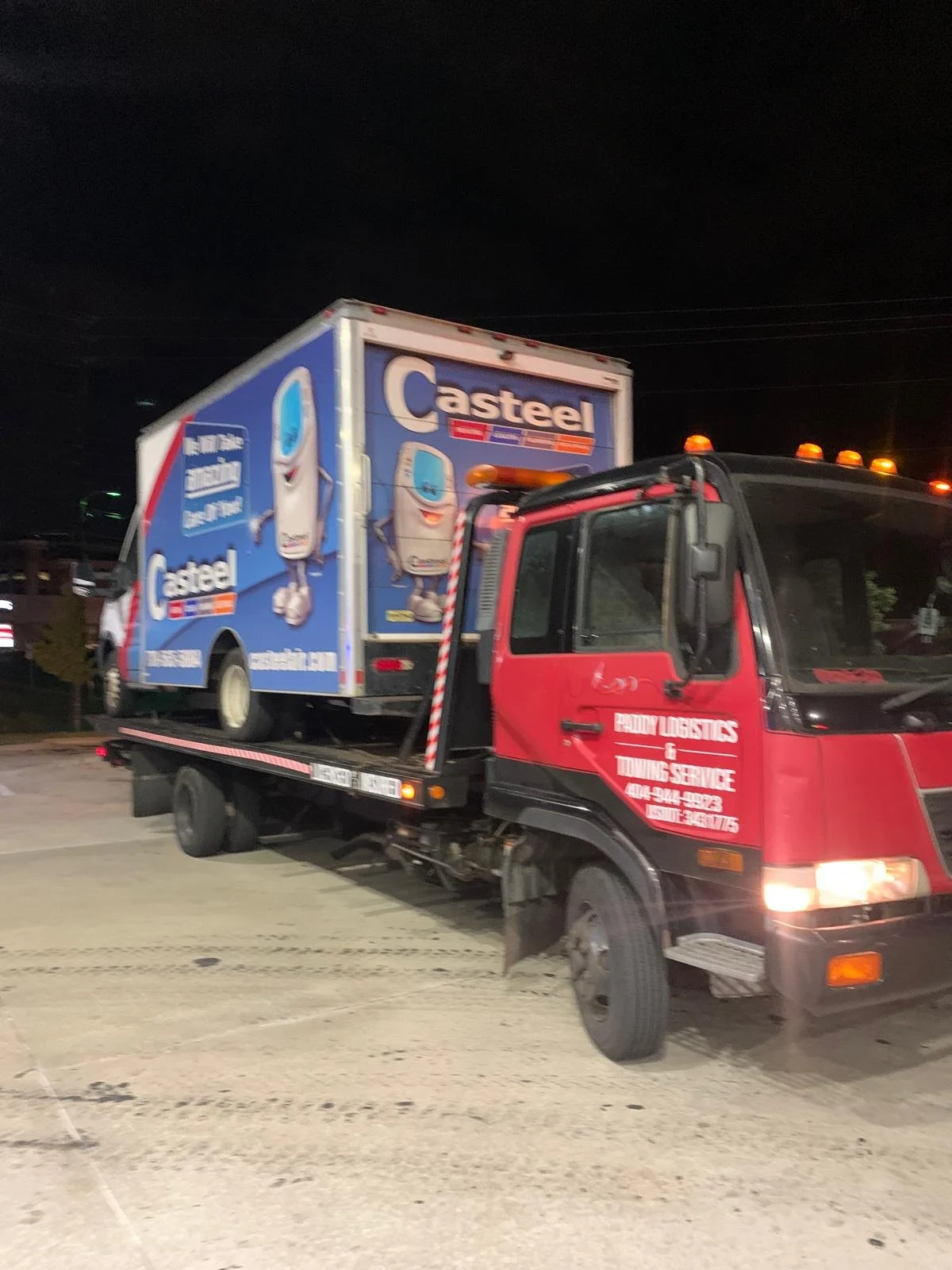 Red Paddy Logistics roadside assistance tow truck carrying a Casteel-branded box truck at night
